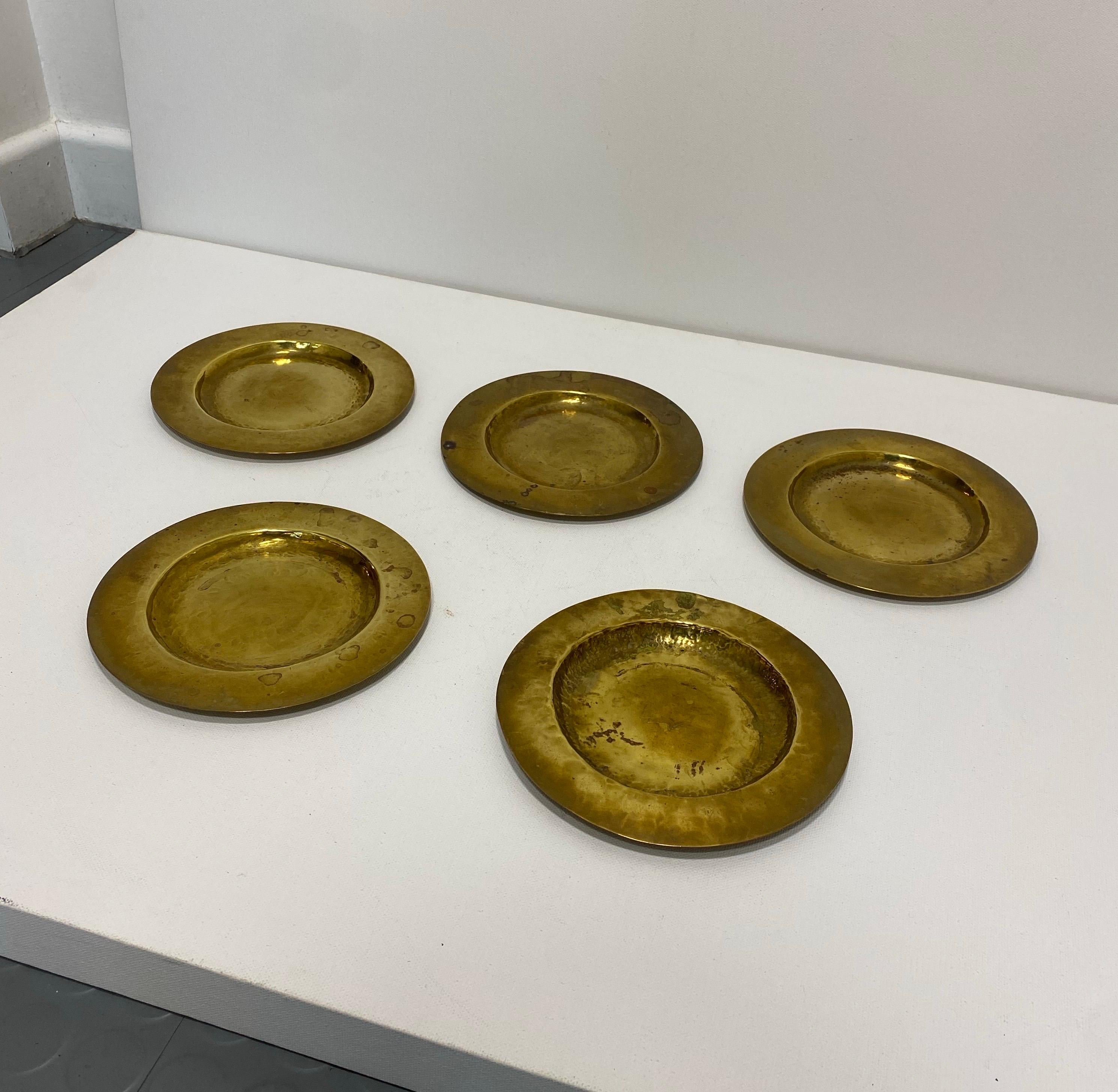 Un bel ensemble de cinq petites assiettes rondes en laiton martelé de la taille d'un dessert. 
Chaque assiette présente un centre légèrement concave et un bord surélevé. La texture martelée à la main leur confère une qualité rustique et artisanale