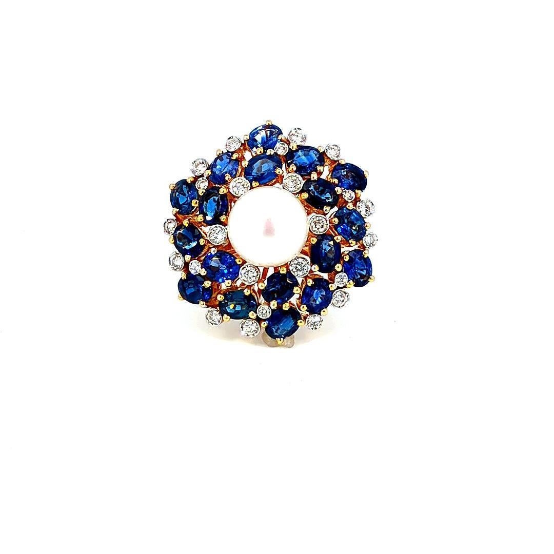 This striking cluster ring by Iris Fine Jewelry is a captivating masterpiece, featuring a harmonious blend of luxurious gemstones. At its heart lies a 10.0 carat round pearl, exuding a lustrous white sheen that commands attention. Surrounding the