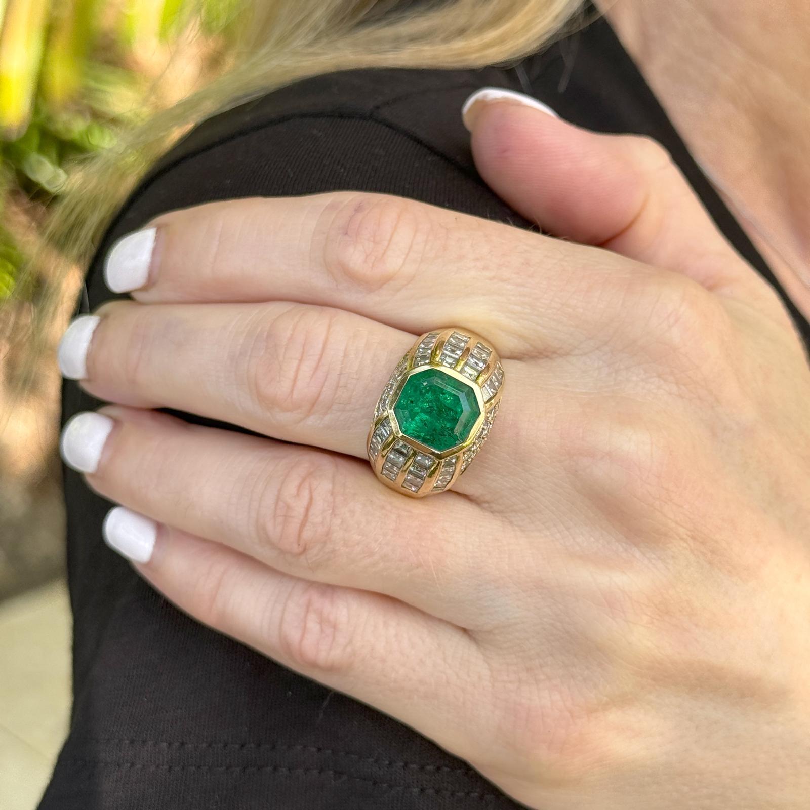 Cette luxueuse bague en or jaune 18 carats, ornée d'émeraudes de Colombie et de diamants, est un chef-d'œuvre d'élégance raffinée. En son centre se trouve une magnifique émeraude colombienne d'environ 5,03 carats, sertie pour mettre en valeur sa