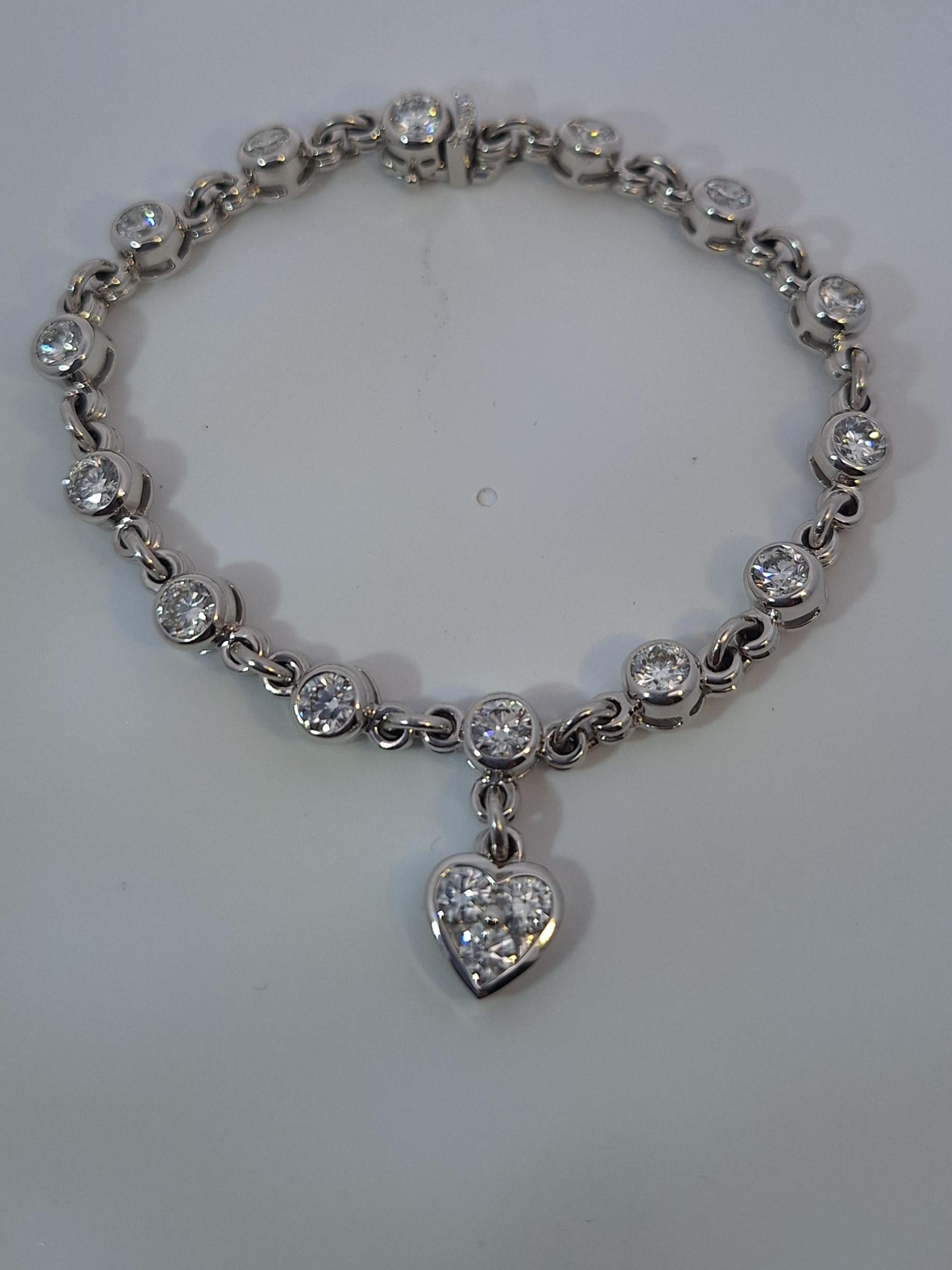 18Kt White Gold Diamond bracelet, features fourteen bezel set round brilliant cut diamonds and one hanging heart charm set with round diamonds. Total diamond weight is approximately 5.00 carats, E-F color and VS clarity. Length is approx. 6.5