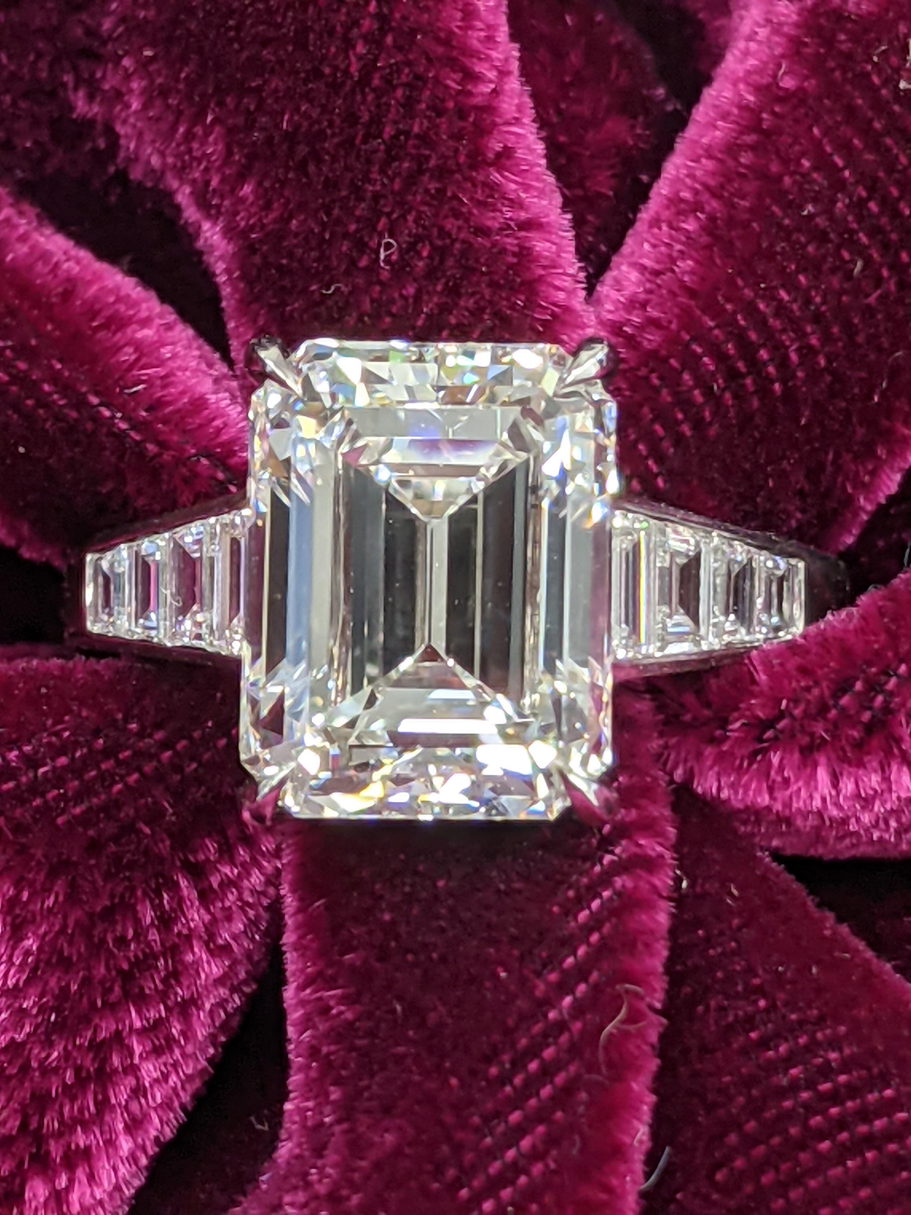 Center diamond is 5.01 carats emerald shape, H color, VVS2 clarity (GIA Report upon request) mounted in a one-of-a-kind, spectacular platinum setting with eight small trapezoids (0.62ct), four flanking each side of the diamond in a stunning