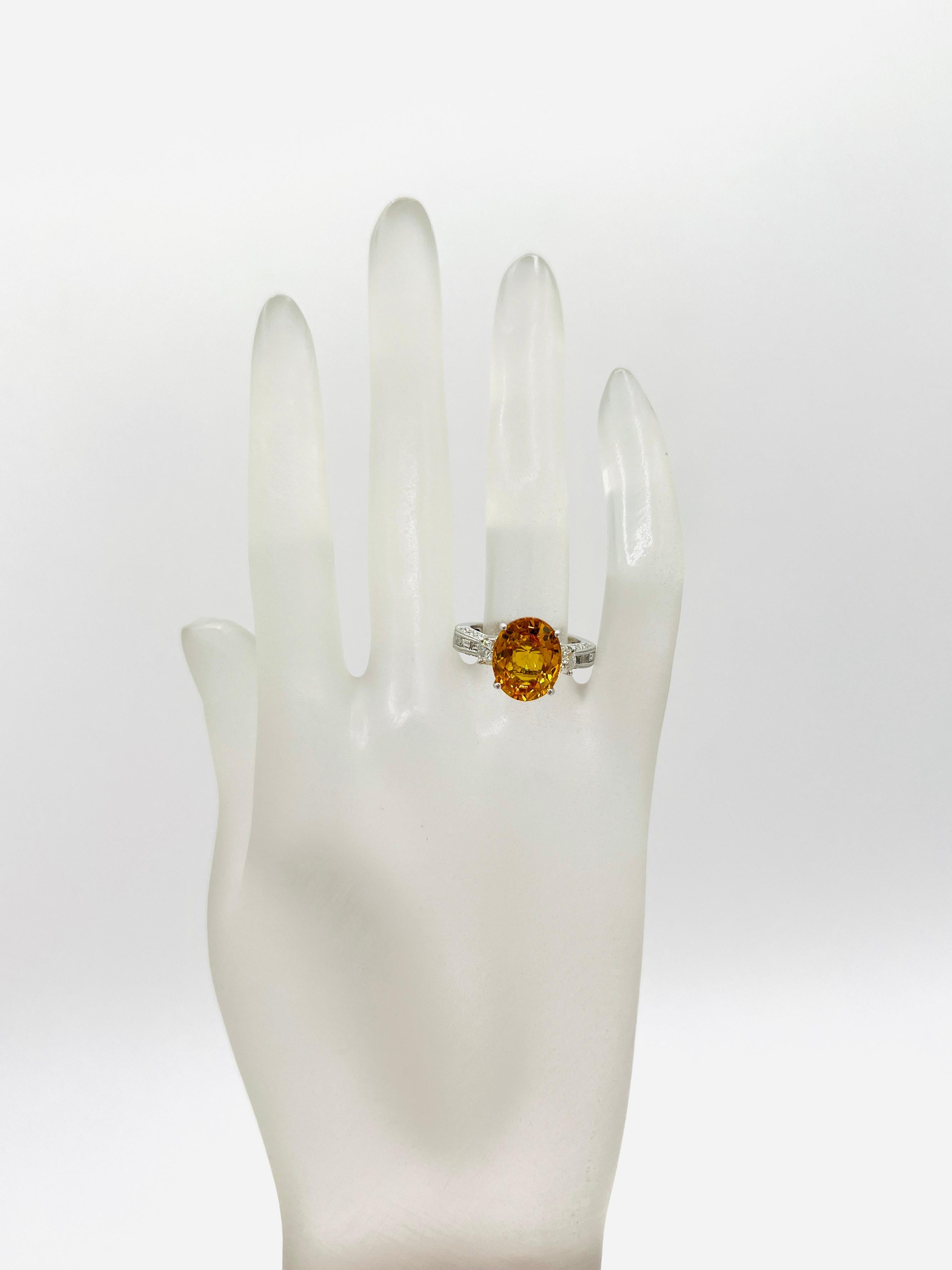 Magnifique saphir orange ovale de 5,50 ct. avec des diamants blancs de bonne qualité en forme de demi-lune, baguettes et ronds.  Fabriqué à la main en or blanc 18 carats.  Bague taille 6.75.