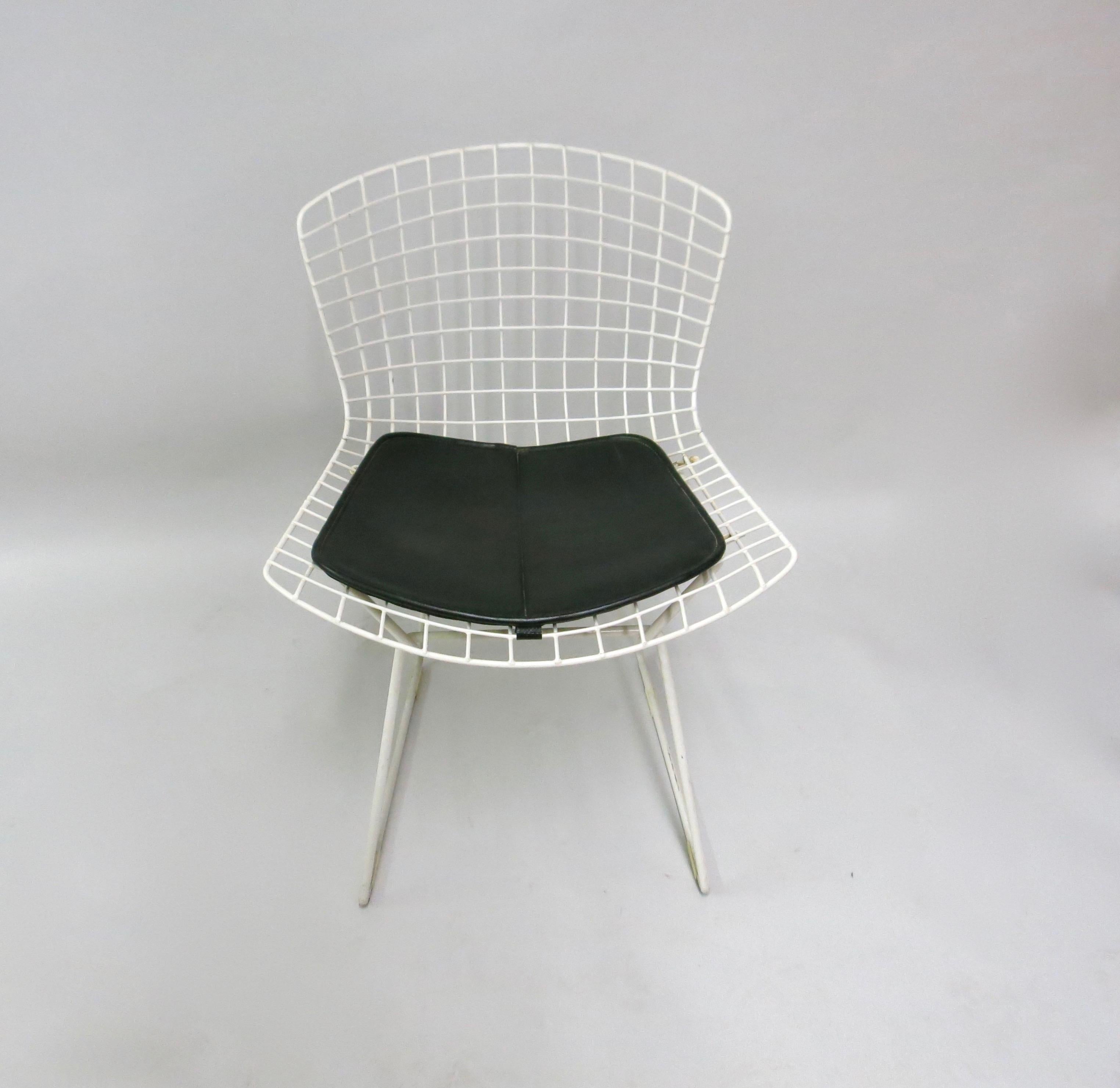 5 white side chairs by Harry Bertoia for Knoll with black leatherette seat with snap button closures on the bottom to attach the cushion to the frame.