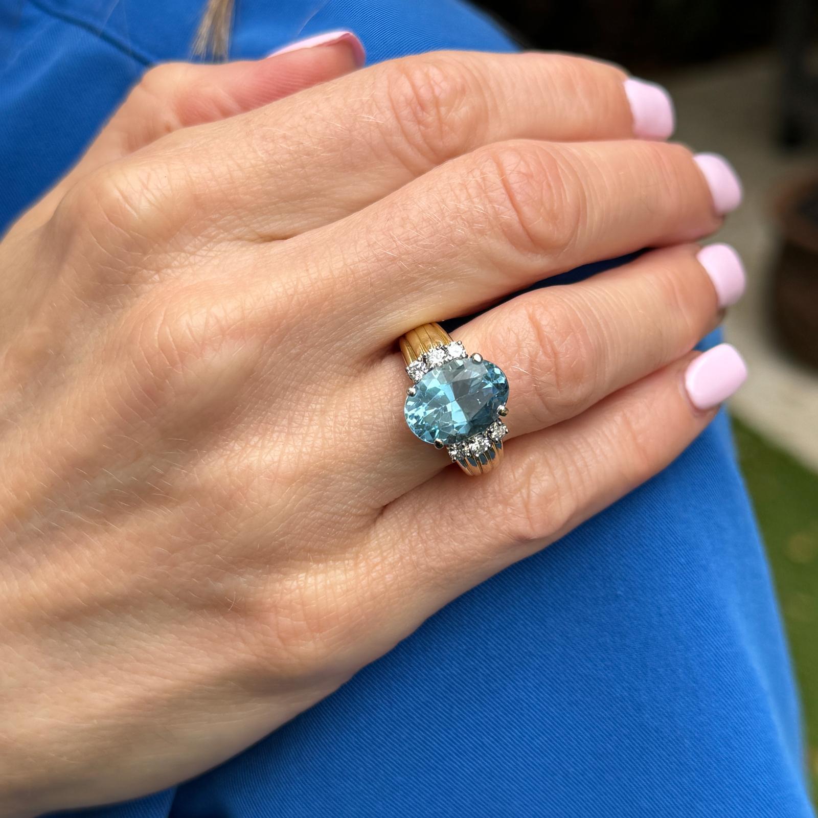 This graceful 18 karat yellow gold ring features a stunning oval aquamarine of approximately 5.00 carats, displaying a serene, ocean-blue hue. Flanking the center stone are six round brilliant-cut diamonds with a total weight of approximately 0.33