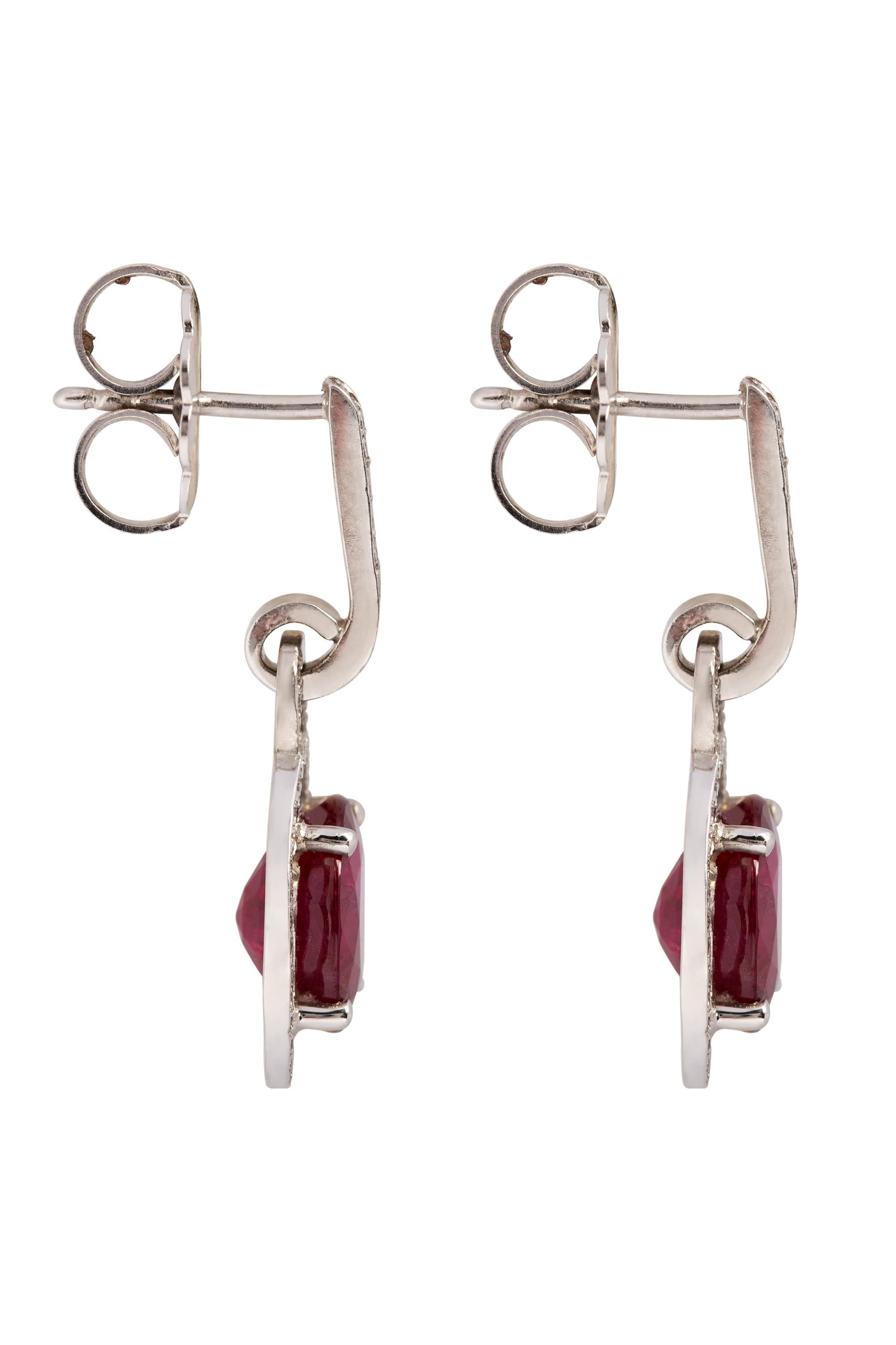 These refined and glamorous 1 inch drop earrings are composed of two deep red oval rubies weighing approximately 5 carats in total, radiating from within frames of glittering pave diamonds that dangle delicately from lines of more sparkling pave