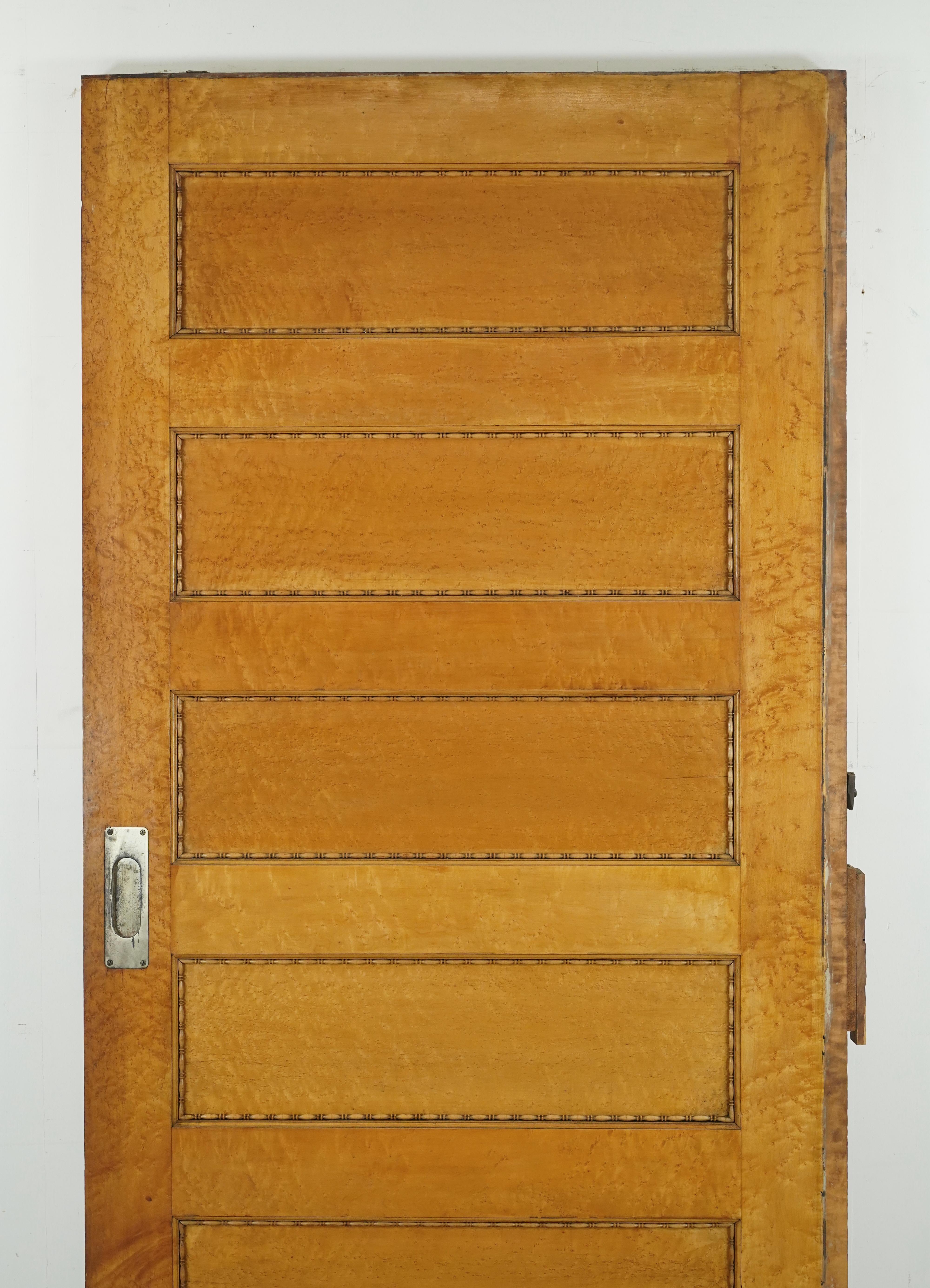 Pocket door with five horizontal panels in a medium and light stain finish. Both sides have decorative trimmed panels. The door is in good solid condition with surface wear along the edges and trim pieces missing. The original recessed brass pulls