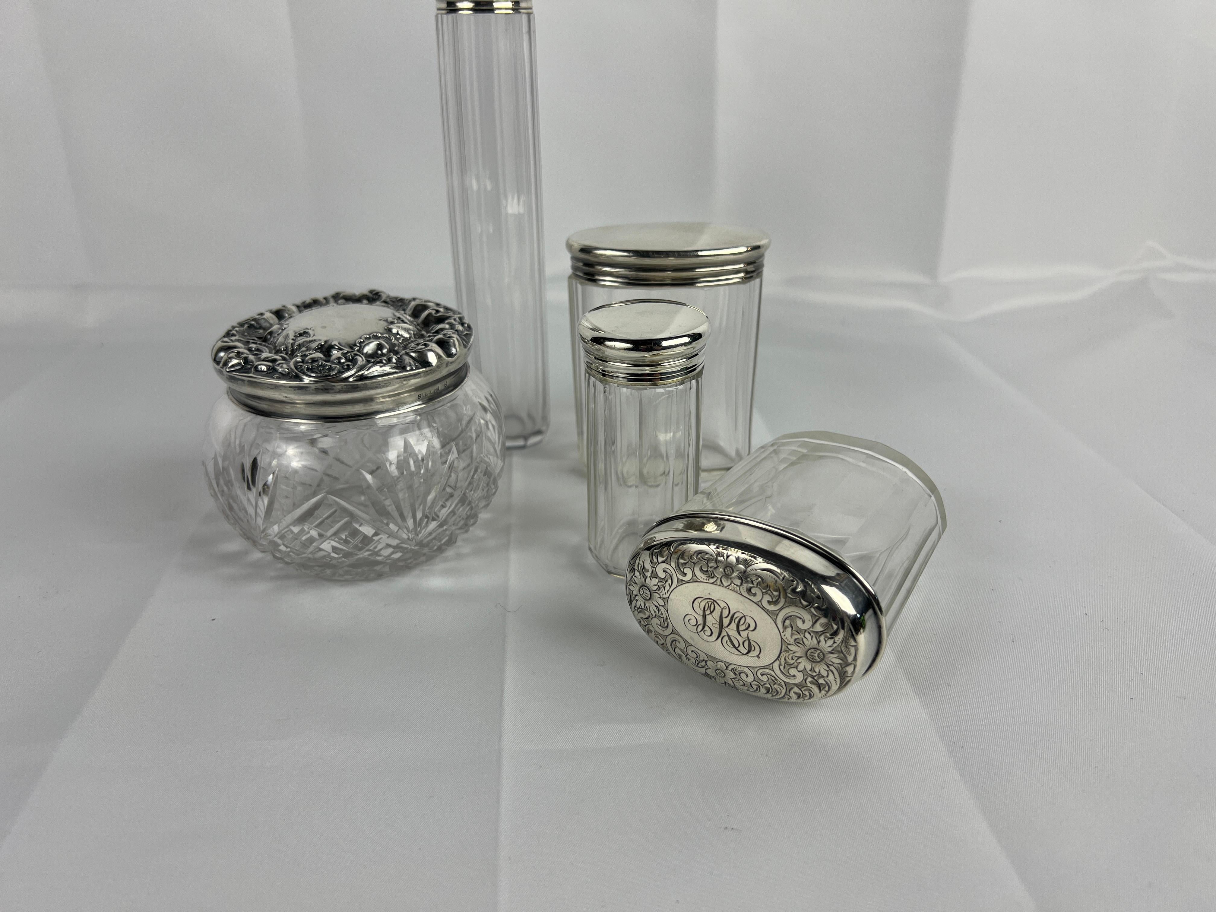 Questa collezione di cinque pezzi di vasi da toilette in argento sterling e cristallo mette in mostra un'armoniosa miscela di artigianato inglese e americano, che riflette l'eleganza senza tempo del design del XIX e dell'inizio del XX secolo. Ogni
