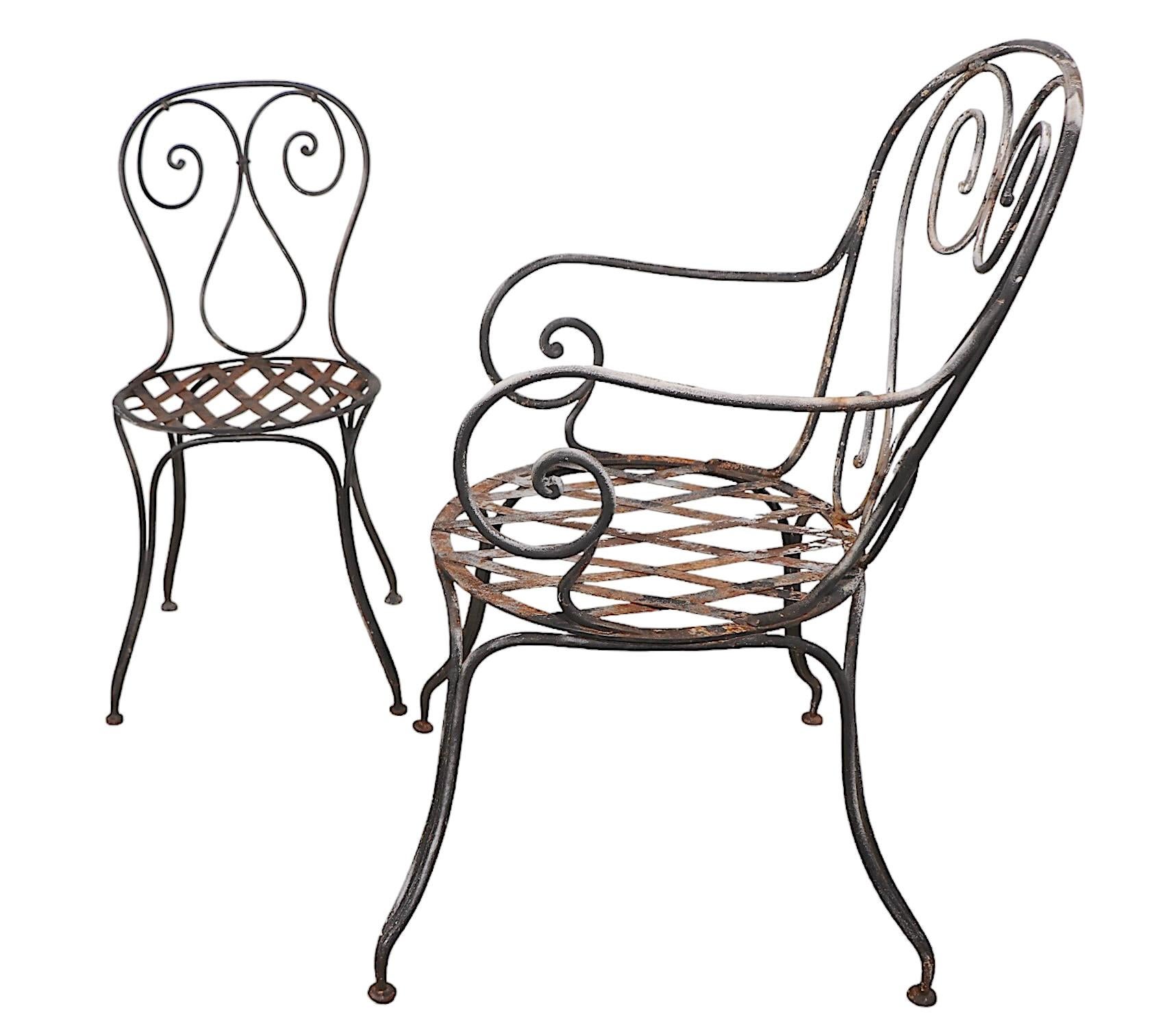 Charming French wrought iron bistro set, having four chairs and a diminutive cafe style table. The chairs include three side, and one arm chair, which  feature graceful curvilinear backs, legs, and  metal strap basket weave seats.
 The set is in