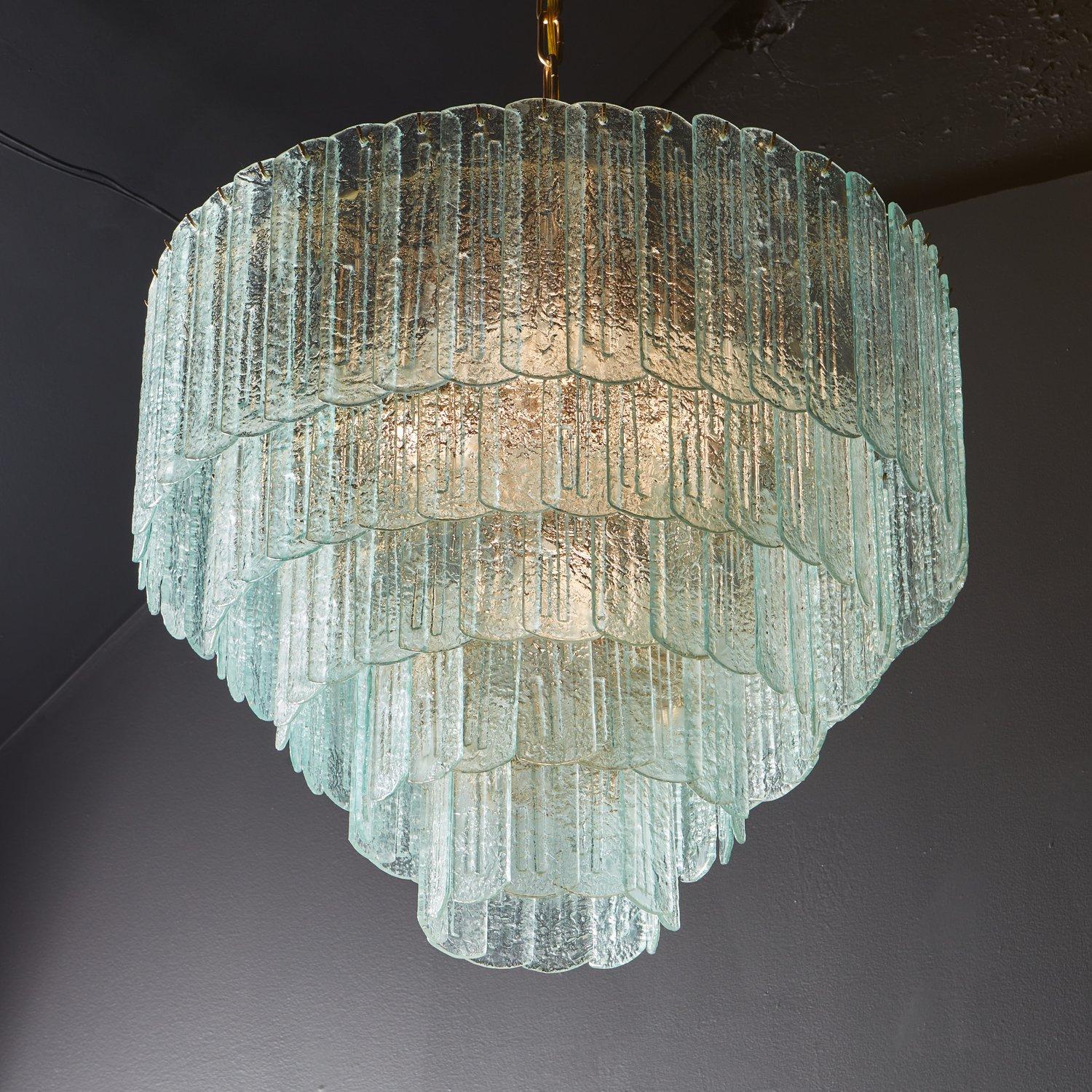 A stunning vintage chandelier featuring over 100 handblown Murano frosted glass pieces with curved edges and textural linear details. The glass hangs in five tiers from a bronze frame and has a beautiful green hue. Sourced in Italy, 20th
