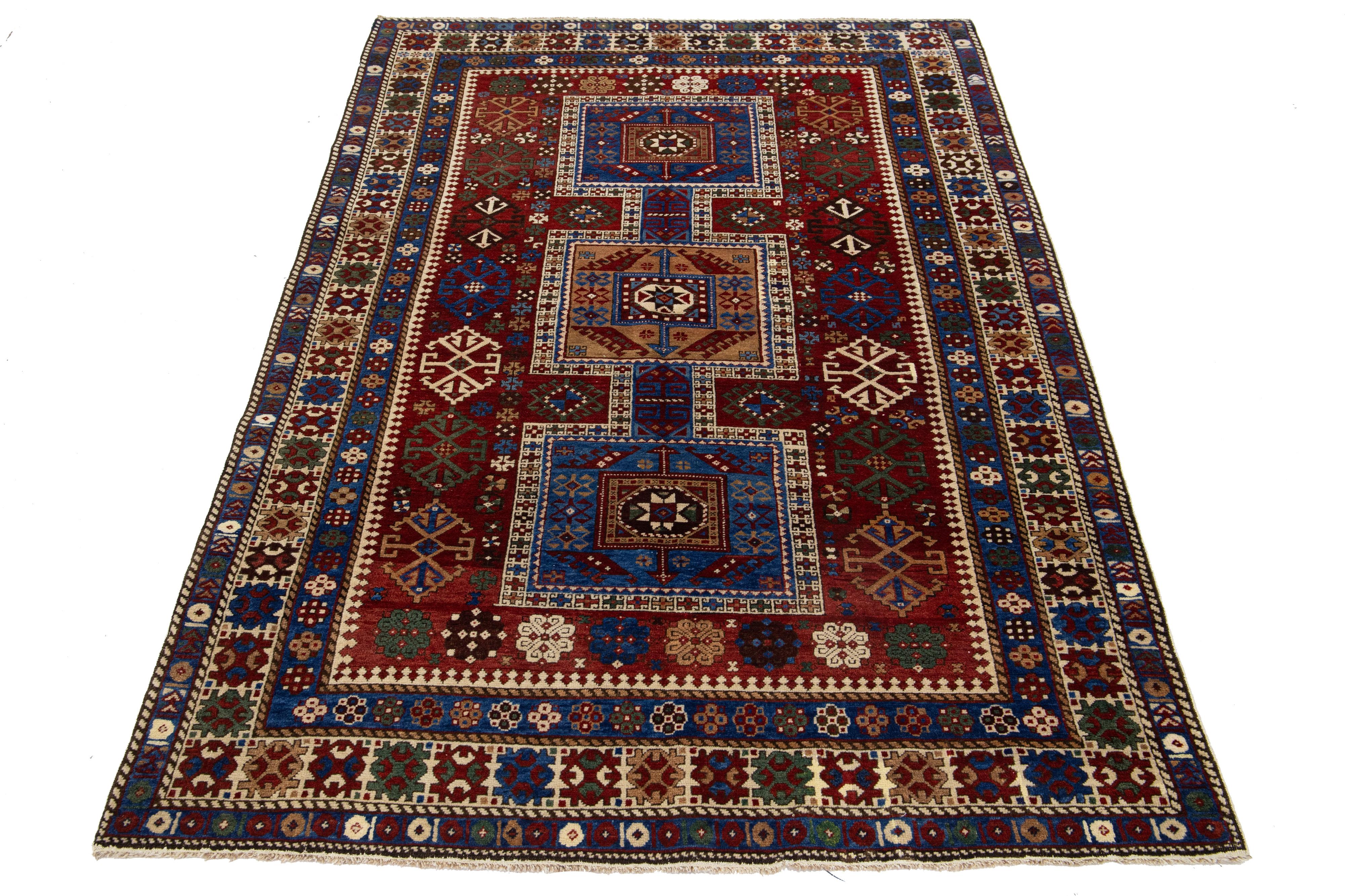 This handcrafted Kazak wool rug features a rich red palette adorned with delicate embellishments in shades of brown, green, blue, and beige. It also showcases an intricate geometric pattern that covers the center of the piece.

This rug measures