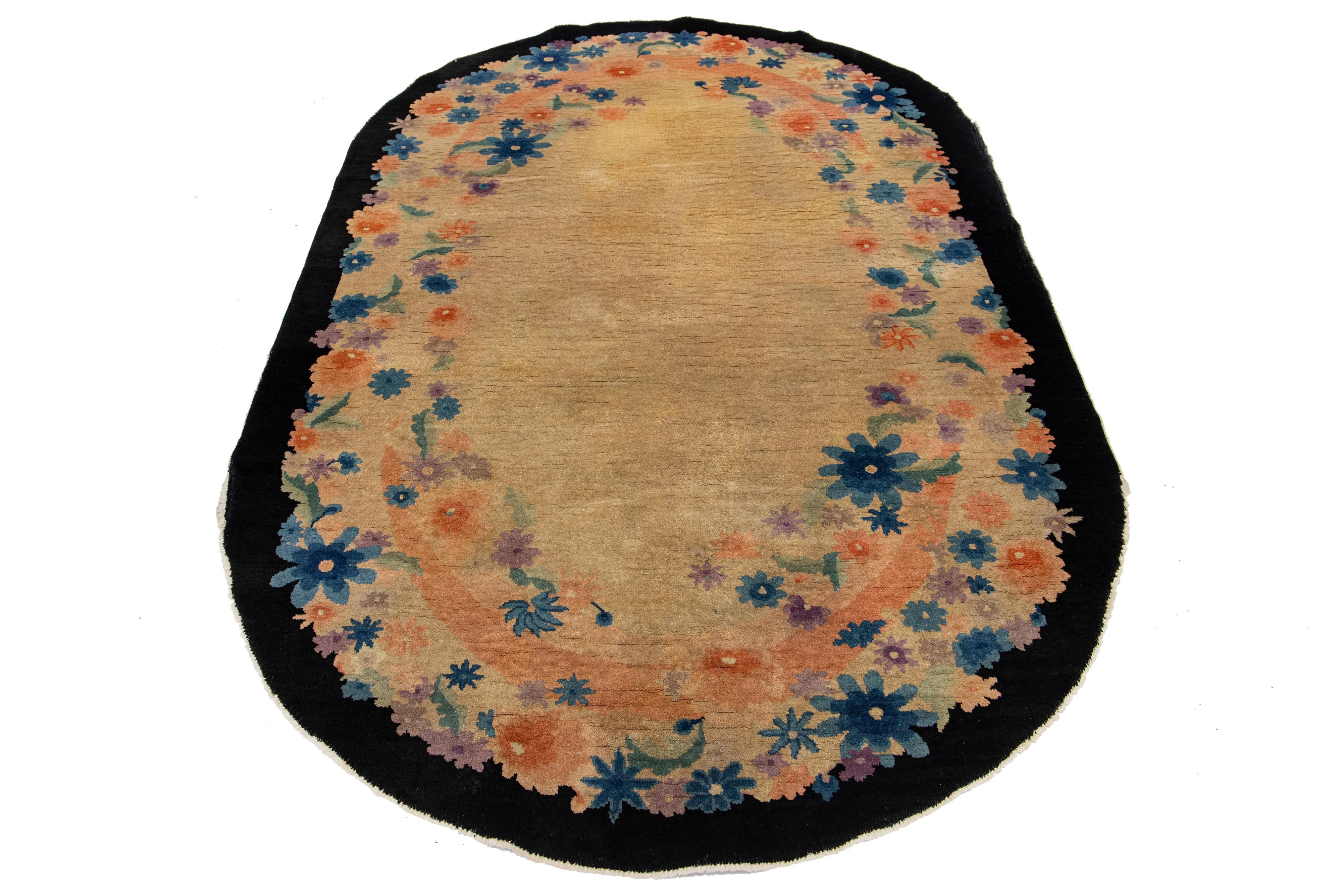 Un antico tappeto cinese ovale annodato a mano presenta uno sfondo marrone chiaro bordato di nero, ornato da un ricco disegno floreale all-over in più colori.

Questo tappeto misura: 5' x 7'7