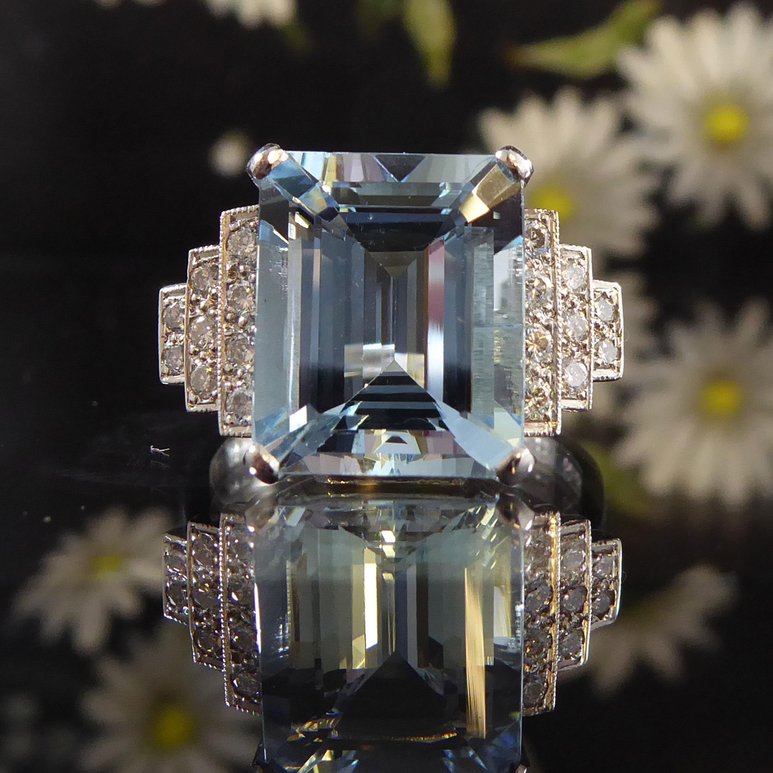 Ein mit Aquamarin und Diamanten besetzter Kleiderring, in dessen Mittelpunkt ein achteckiger Aquamarin mit Stufenschliff steht. Er misst 12,15 mm x 10,10 mm x 5,97 mm und ist in einer weißen, rechteckigen Fassung mit doppelter Lünette gefasst.  Auf