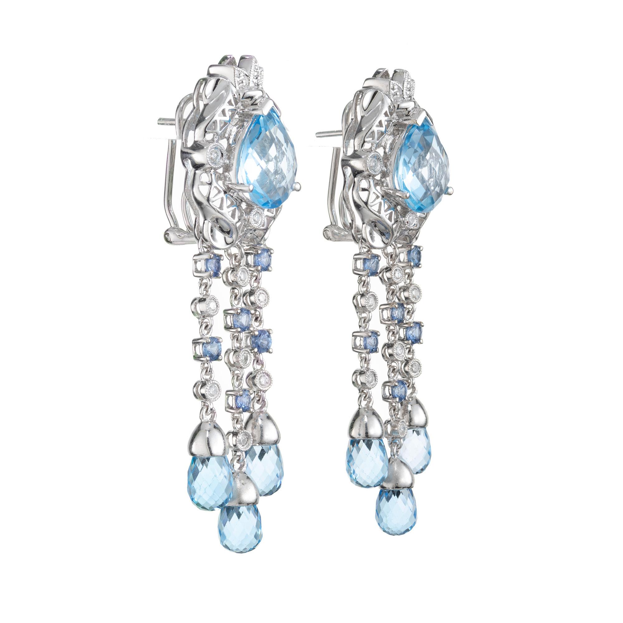 Réalisées à la perfection, ces boucles d'oreilles pendantes sont ornées de superbes topazes bleues magnifiquement mises en valeur par d'éblouissants diamants et saphirs, dans une monture en or blanc 14 carats. Au centre de chacune de ces boucles