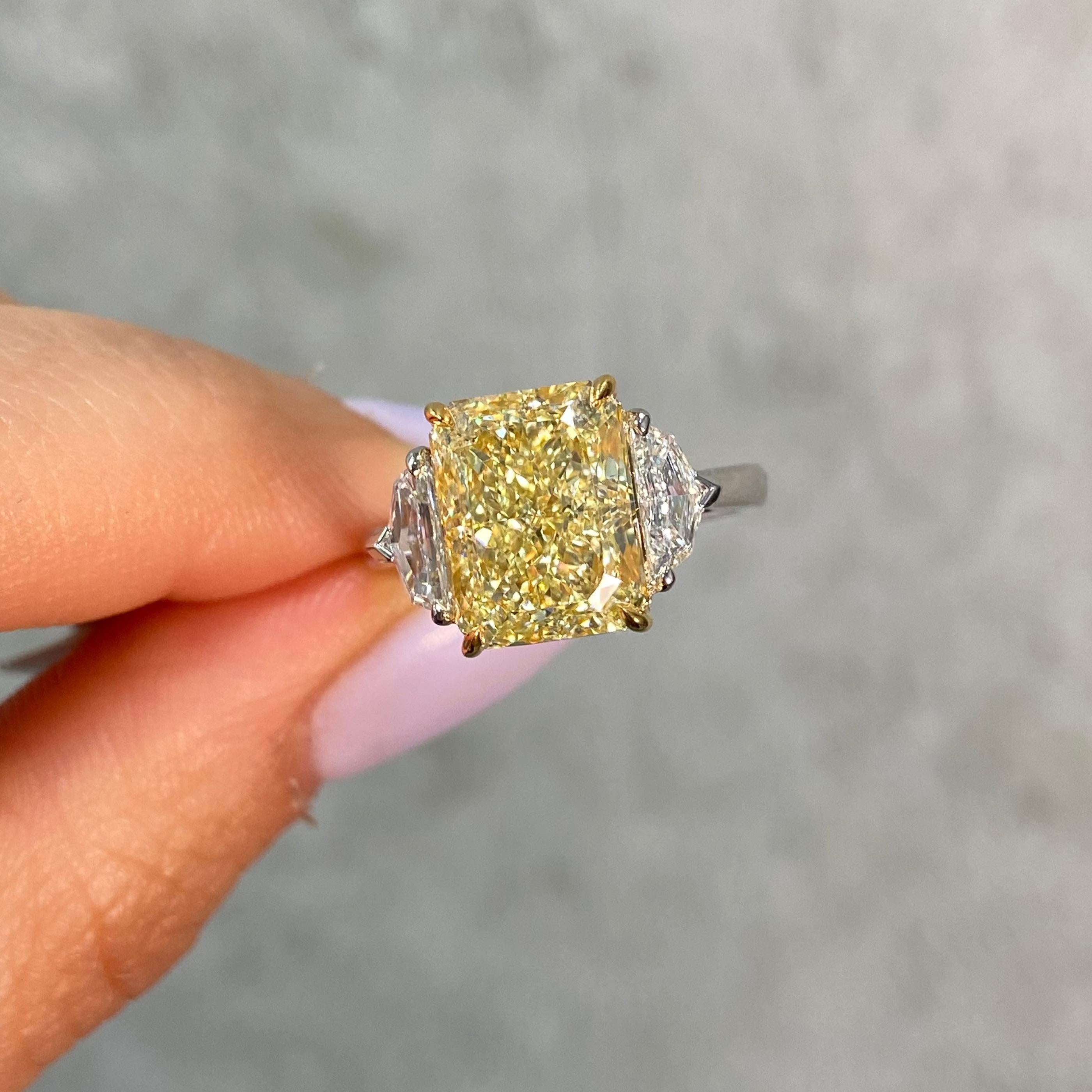 Manche Dinge sind zu dritt einfach besser. Ein Beispiel dafür ist dieser atemberaubende, 5,02 Karat schwere Ring in Fancy Yellow mit länglichem Radiant-Schliff. Der lebendige, sonnenbeschienene Farbton des Mittelsteins wird durch zwei passende