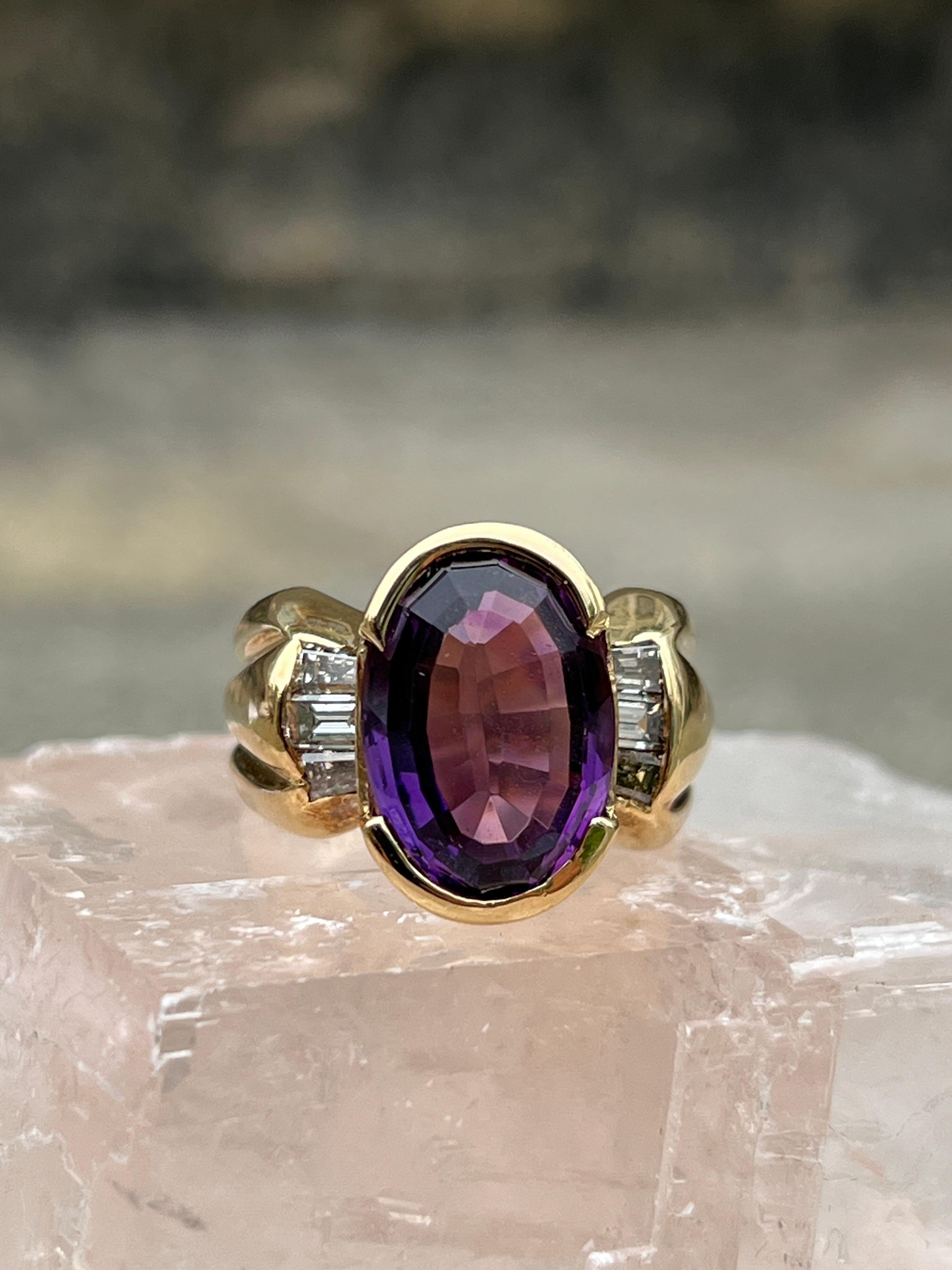 This contemporary cocktail ring is crafted in 14 karat yellow gold and features a striking 5.03 carat oval amethyst, measuring 14x10mm. The vibrant purple gemstone is elegantly accented by six tapered baguette diamonds, totaling approximately 0.41