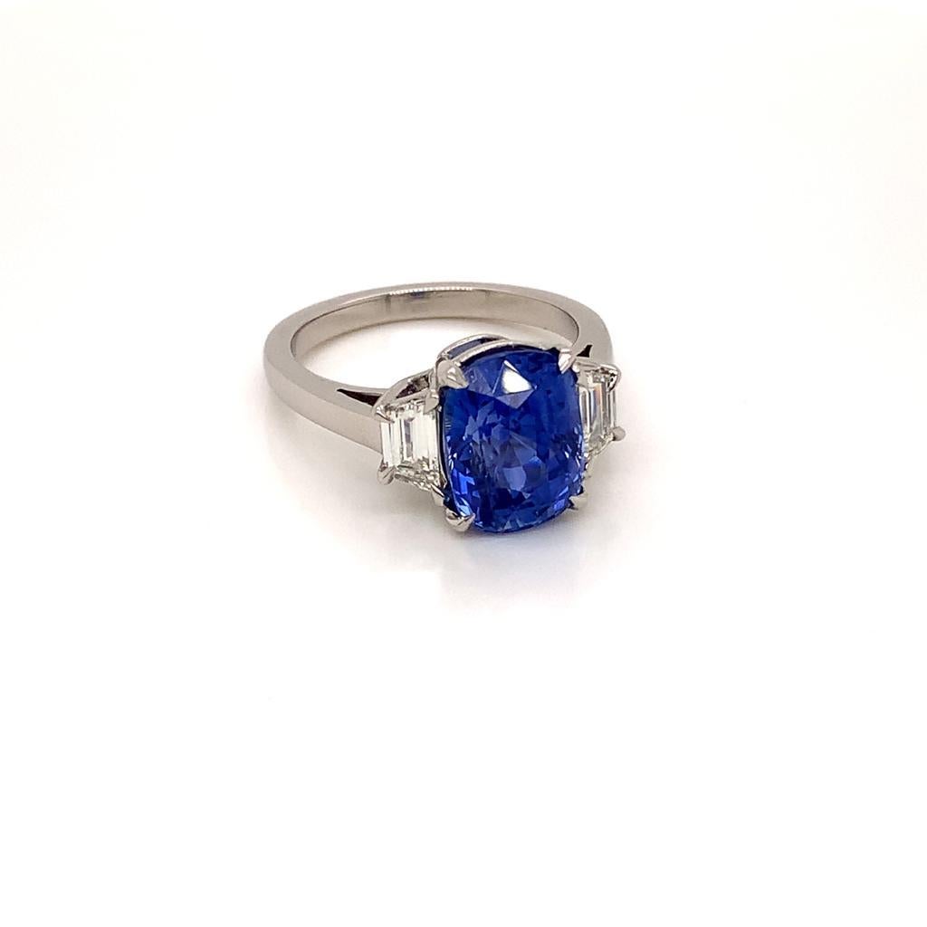 Cette bague contemporaine à trois pierres présente en son centre un saphir bleu de taille coussin d'une beauté immaculée pesant environ 5,04 carats, ainsi qu'un diamant en forme de trapèze de chaque côté, les diamants pesant au total environ 0,53