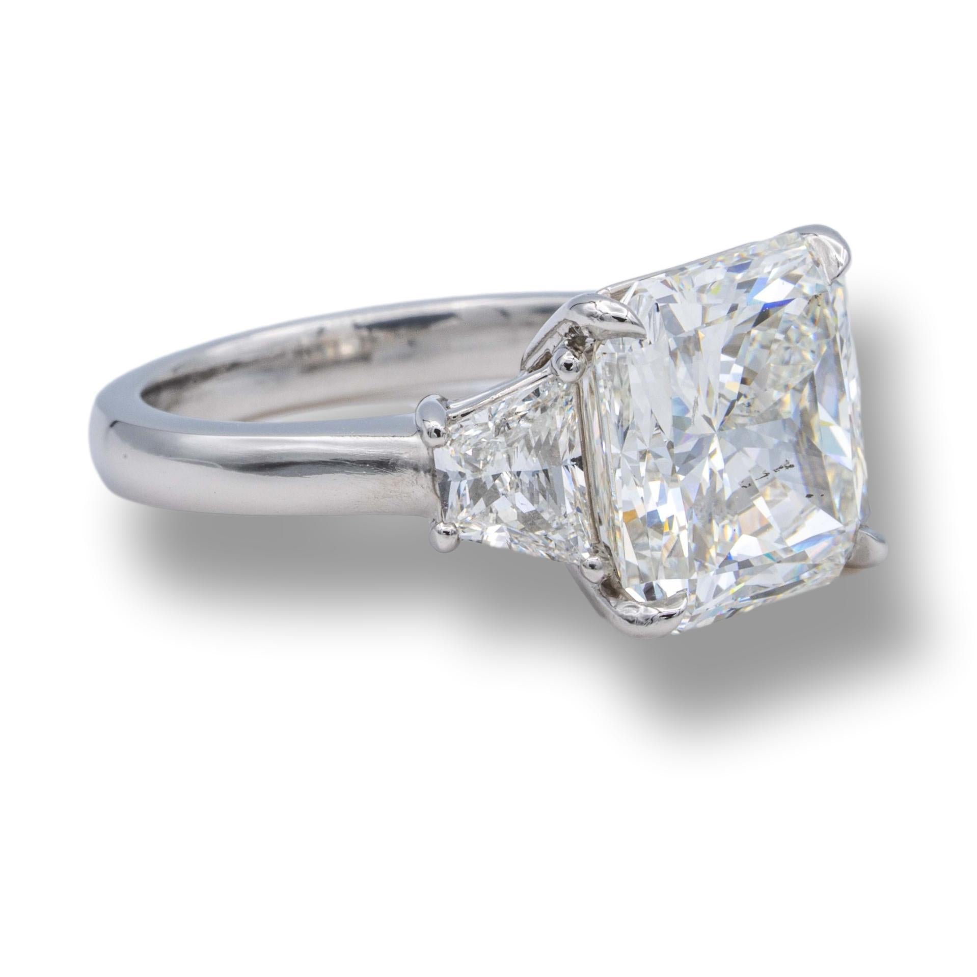 Three stone engagement ring finely crafted in a platinum basket setting with an open gallery showcasing a 5.04 ct radiant cut diamond center I color SI2 clarity flanked by 2 trapezoid diamonds weighing 0.95 carats approximately, I color , VS2