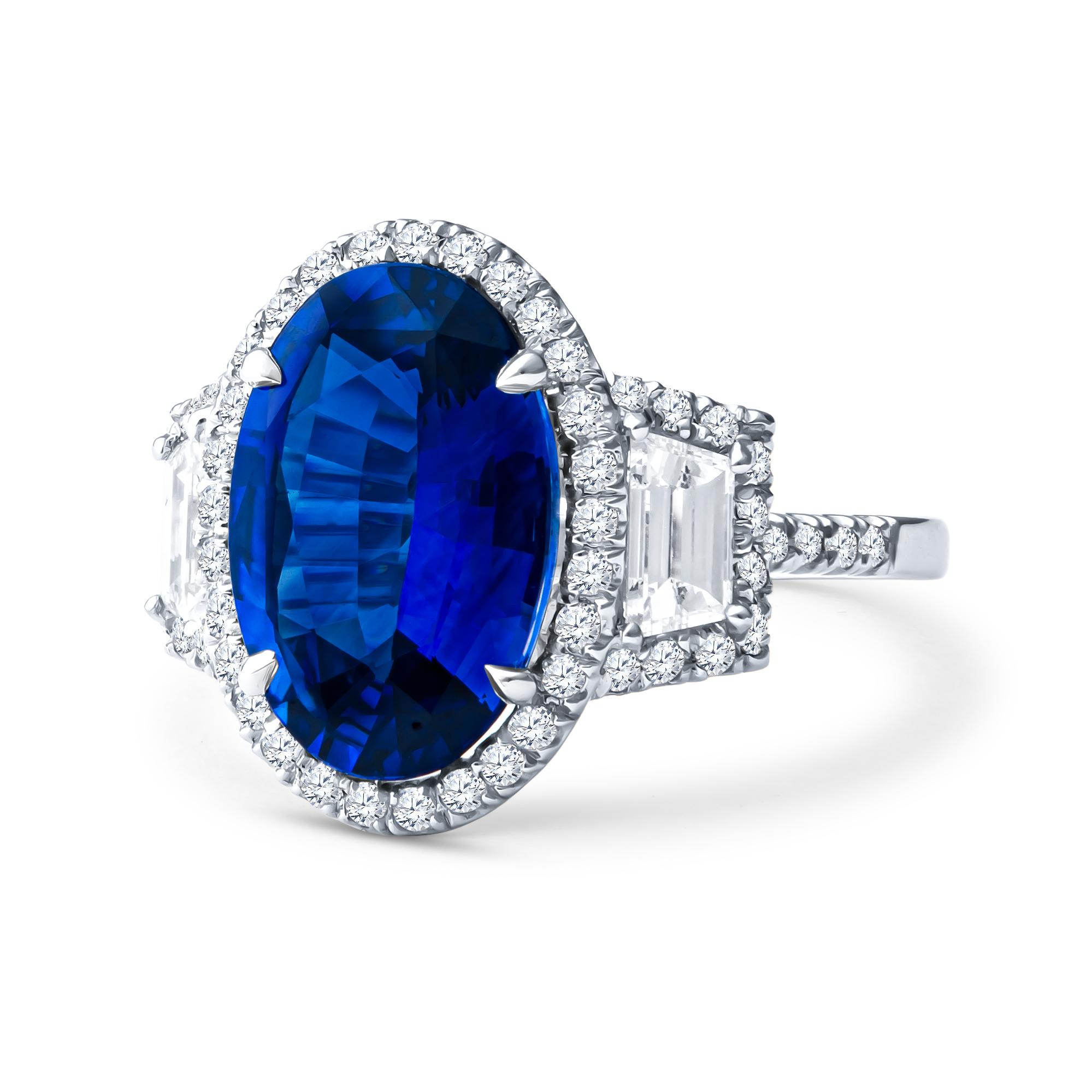 This stunning ring features a 5.04ct oval cut natural blue sapphire, bordered by 2 0.68ct total weight step cut trapezoid diamonds and a 0.50ct total weight round diamond halo. The ring itself is made of platinum, in a size 6.25, which may be