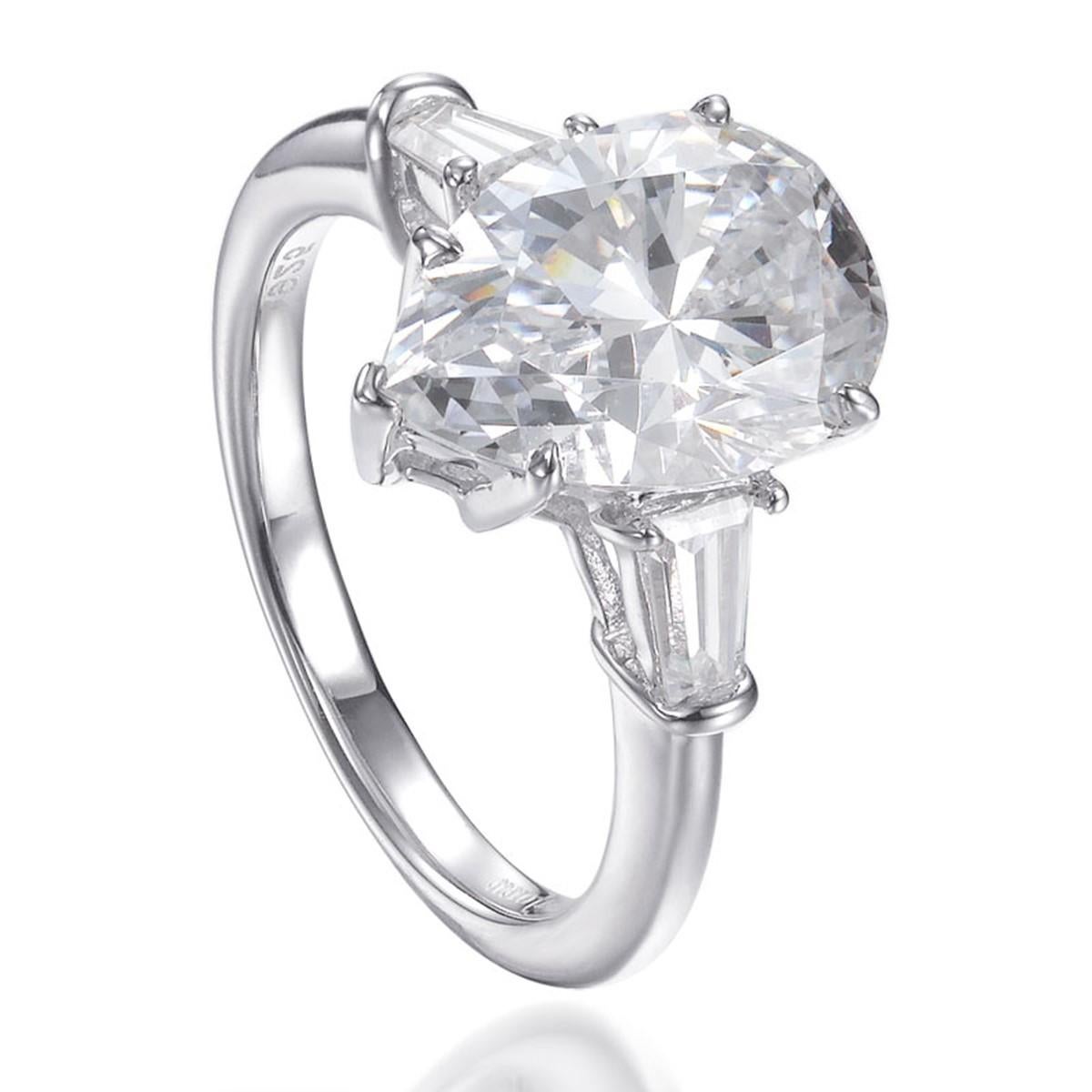 Exceptionally crafted, this classic engagement ring showcases a large 5.05 carat pear shape centre diamond simulant flanked by two beautifully matched tapered baguette cut cubic zirconia, claw set in a 925 sterling silver mount with a high gloss