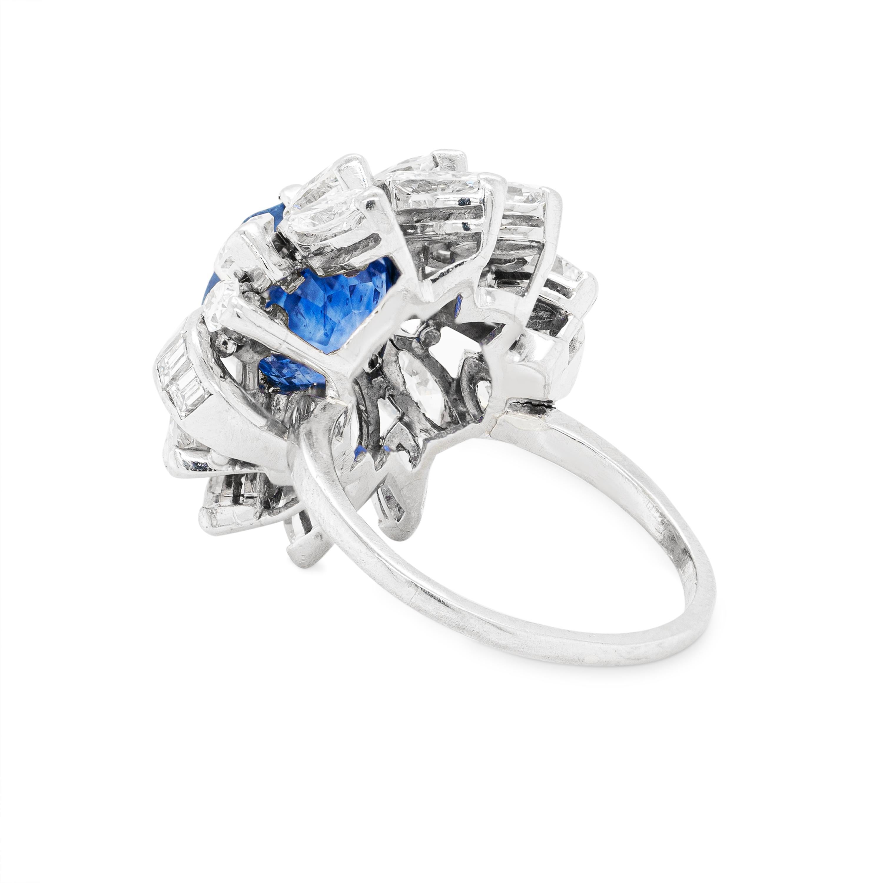 This gorgeous platinum cocktail cluster ring features a beautiful hexagonal step-cut blue sapphire weighing 5.06ct, in a six claw, open back setting. The vibrant gemstone is highlighted by 18 claw set marquise cut diamonds that beautifully complete