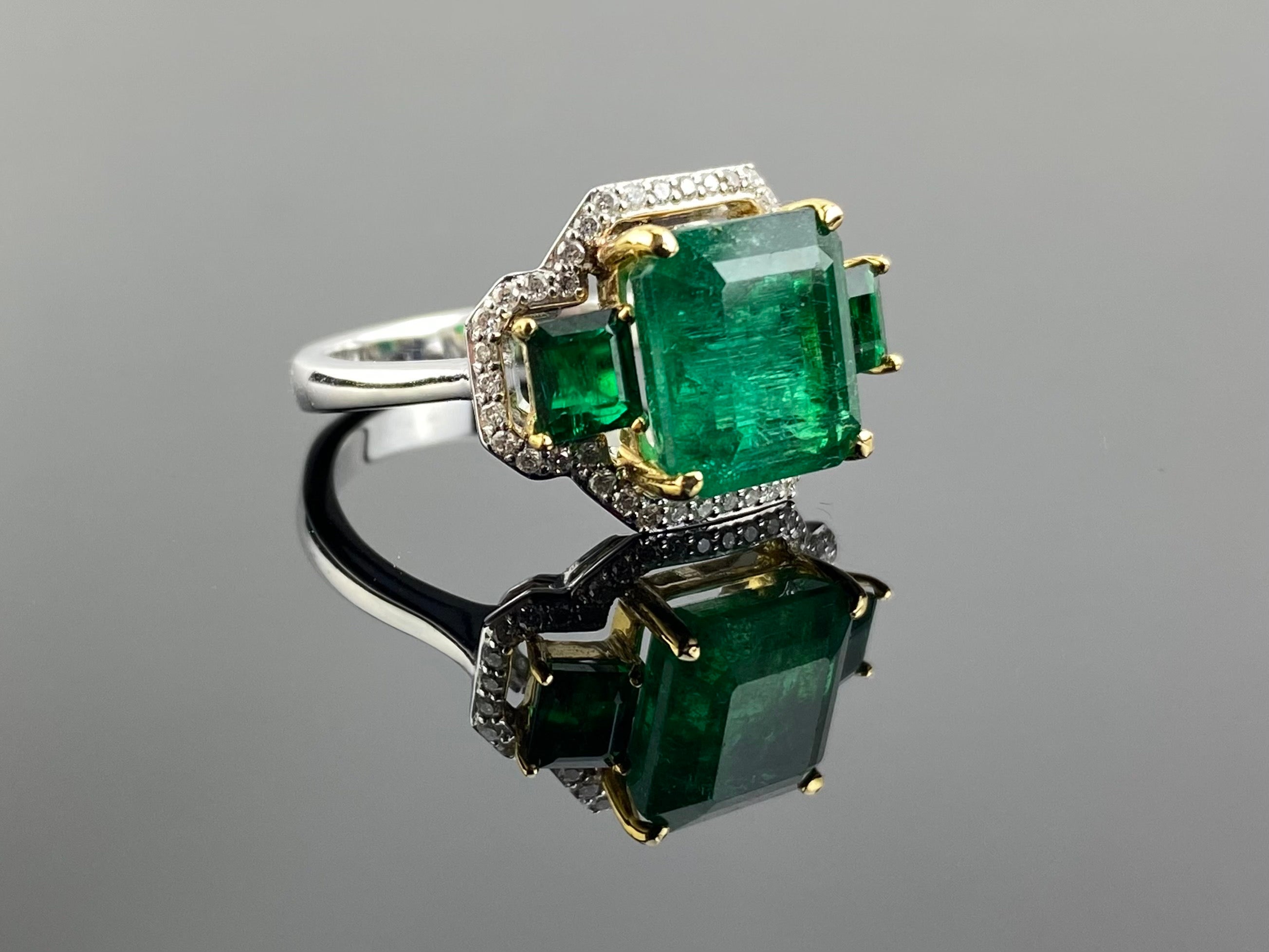 A unique three stone cocktail ring, with 4.31 carat natural Zambian Emerald and 0.76 carat natural Zambian Emerald side stones, with 0.23 carat White Diamond halo all set in solid 18K White Gold. The Emeralds are transparent and have a beautiful