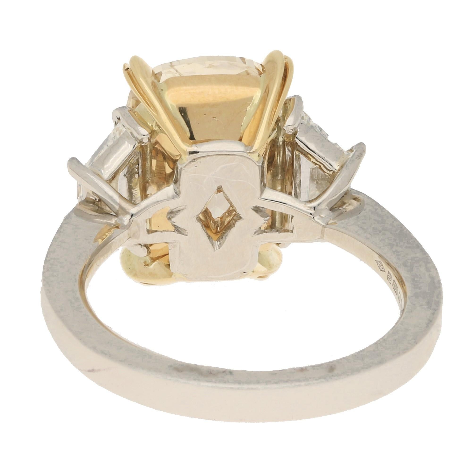 A magnificent fancy yellow cushion brilliant-cut diamond engagement ring in 18-karat yellow gold and platinum. This ring features a breath-taking cushion brilliant-cut diamond four-claw-set to the centre in an openwork yellow gold collet, flanked to