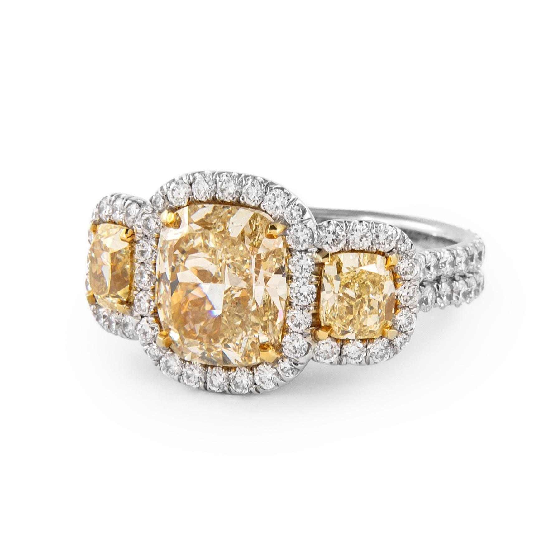 Stunning modern all three stone natural yellow diamond ring with white diamond halo. All three stones natural yellow diamonds.
5.08 carats total diamond weight.
1 cushion diamond, 3.04 carats. Approximately Fancy Yellow color and SI1 clarity. 2