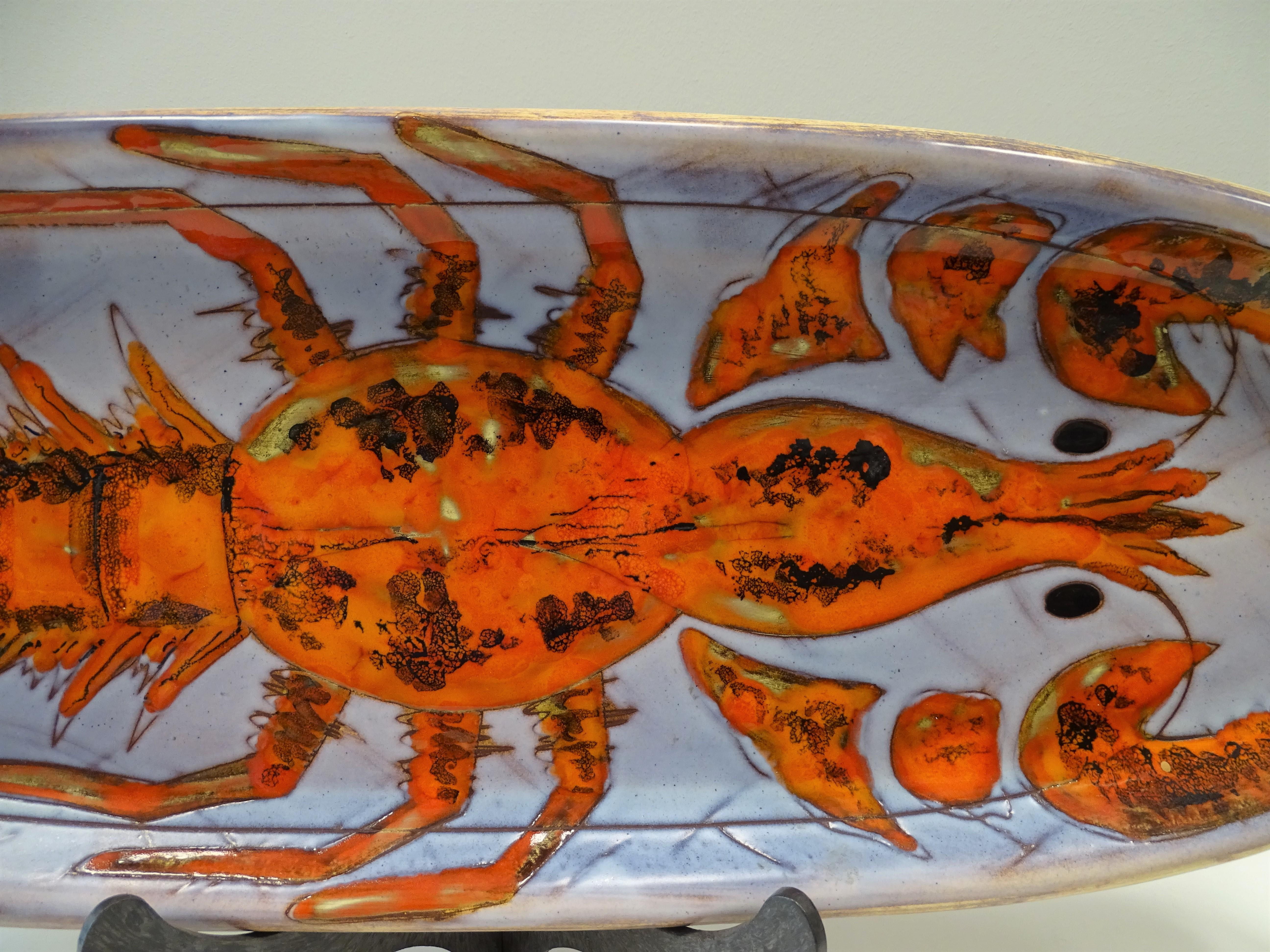 Gorgeous French ceramic tray with an oval profile where a large lobster is represented. With thick lines, the image powerfully draws attention due to its shape and color, both of the crustacean and of the background. It is a manufacture made by