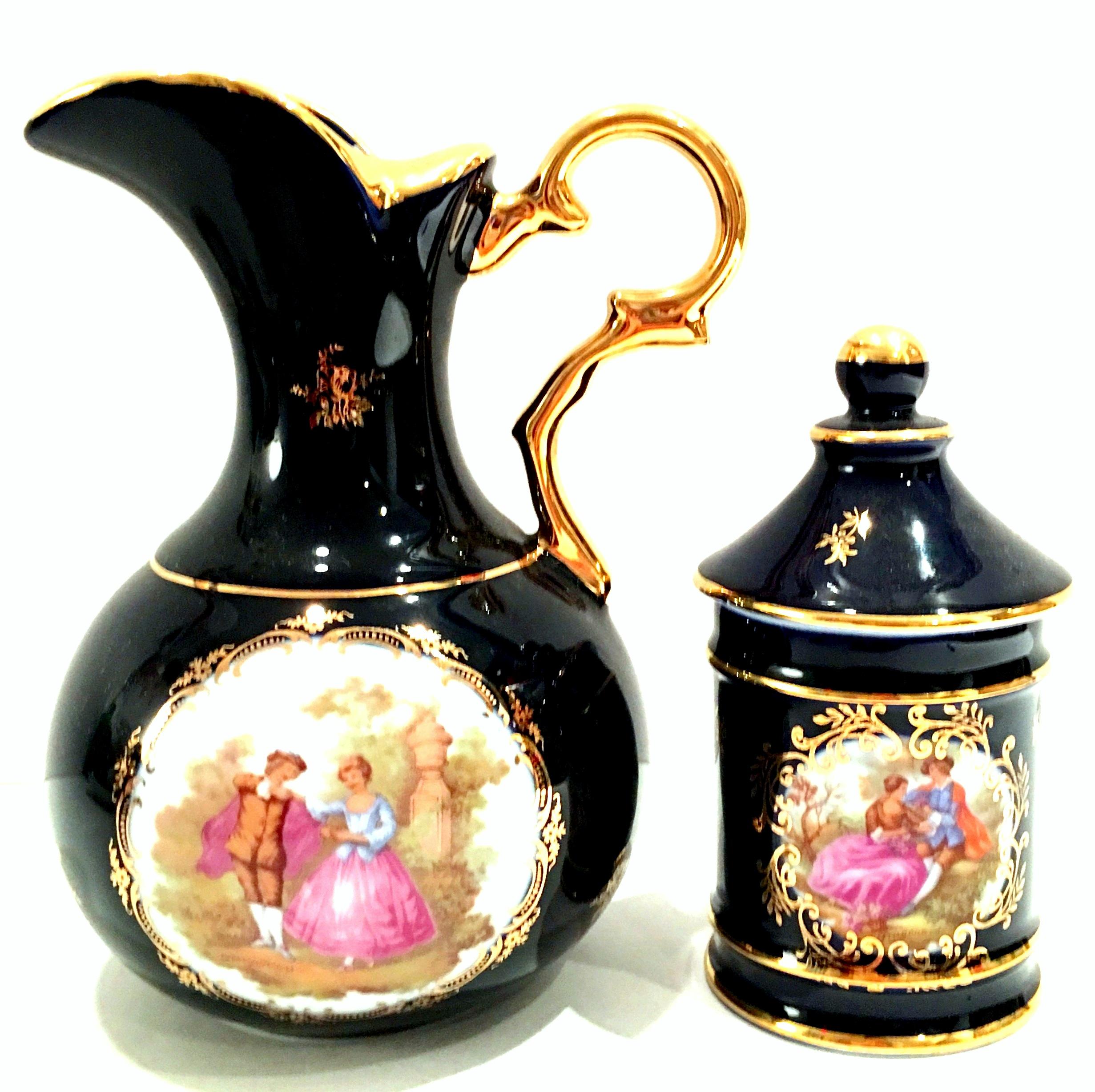 1950'S Cobalt & 22-karat gold detail hand painted Limoges France porcelain handled pitcher and lidded jar. This three-piece set includes a handled beverage pitcher depicting a courting couple and a lidded vanity jar. Each piece is signed on the