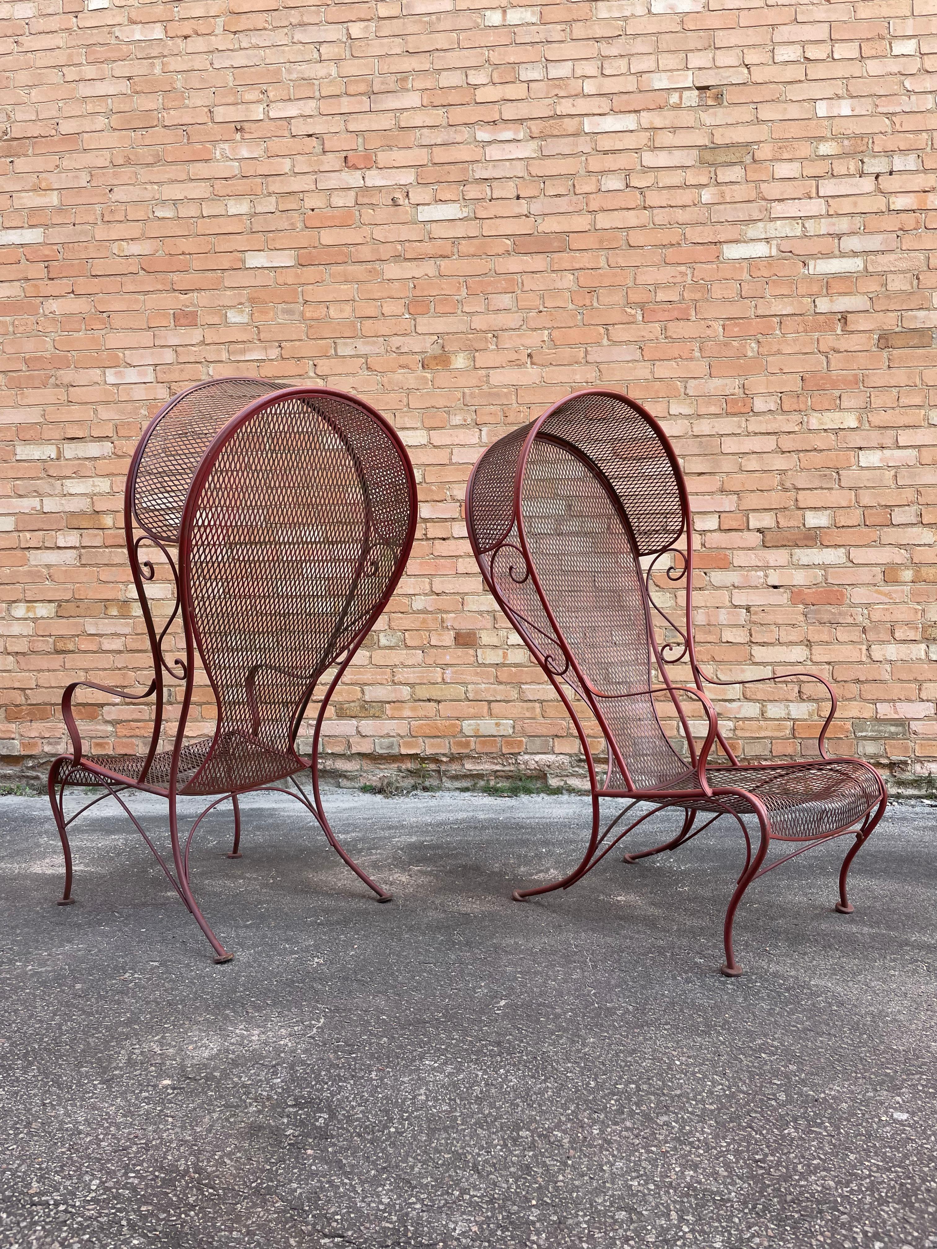 A rare, beautiful pair of Herbert Saiger for Russell Woodard canopy lounge chairs in painted red wrought iron fabricated in the signature Woodard Furniture Company style. Each patio armchair features dramatic oversized canopies flanked by lovely,