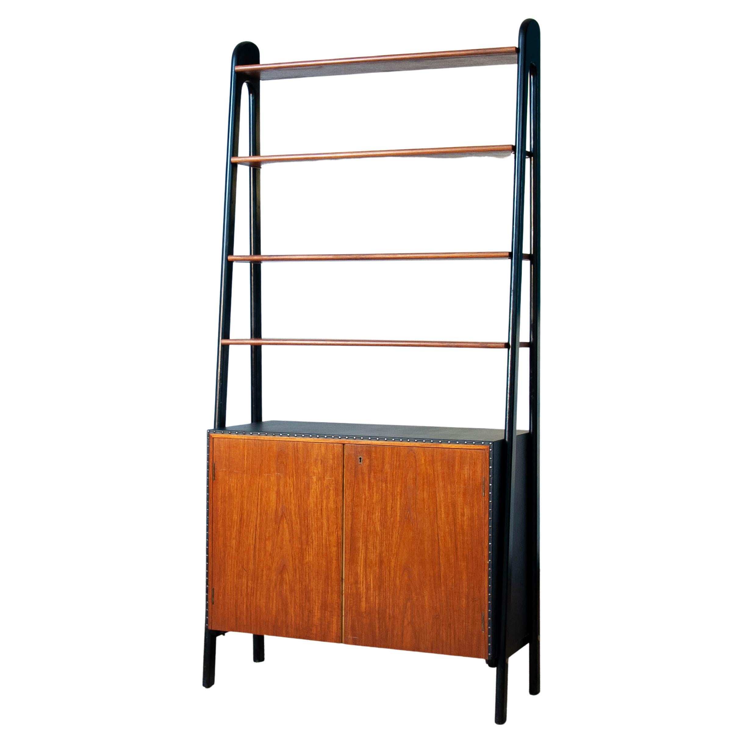 Beautiful bookcase in teak and black faux leather, nailed, and black stands. On top the cabinet has four teak veneered shelfs. The two centered shelfs are adjustable in height. All four shelfs are made to cary heavy weight.
The interior of the