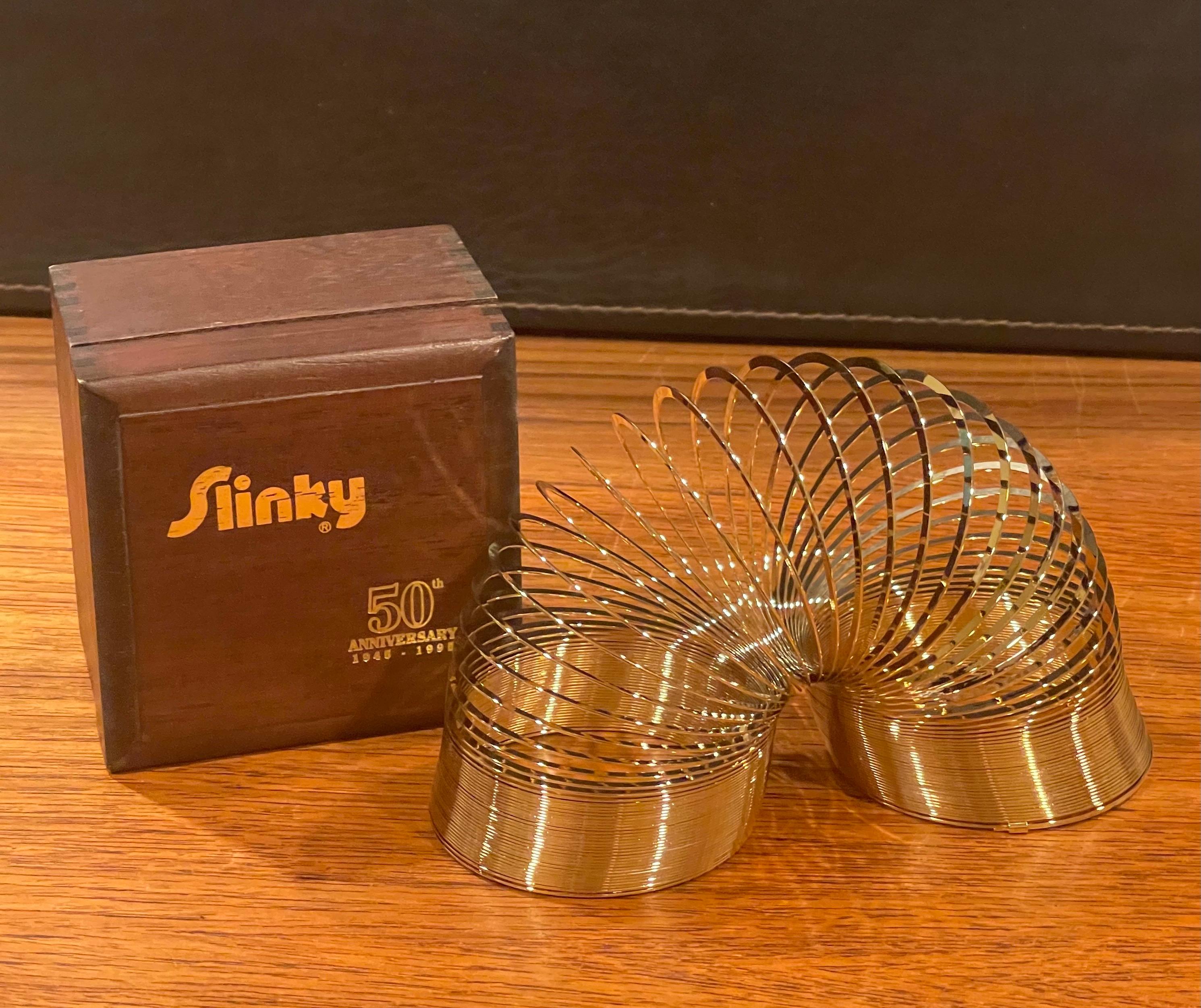 50th Anniversary gold-plated brass Slinky toy in wood box, circa 1995. This item is in brand new condition in the original plastic bag; appears to never have been played with. This Slinky was released in 1995 to celebrate the toy's 50th anniversary;