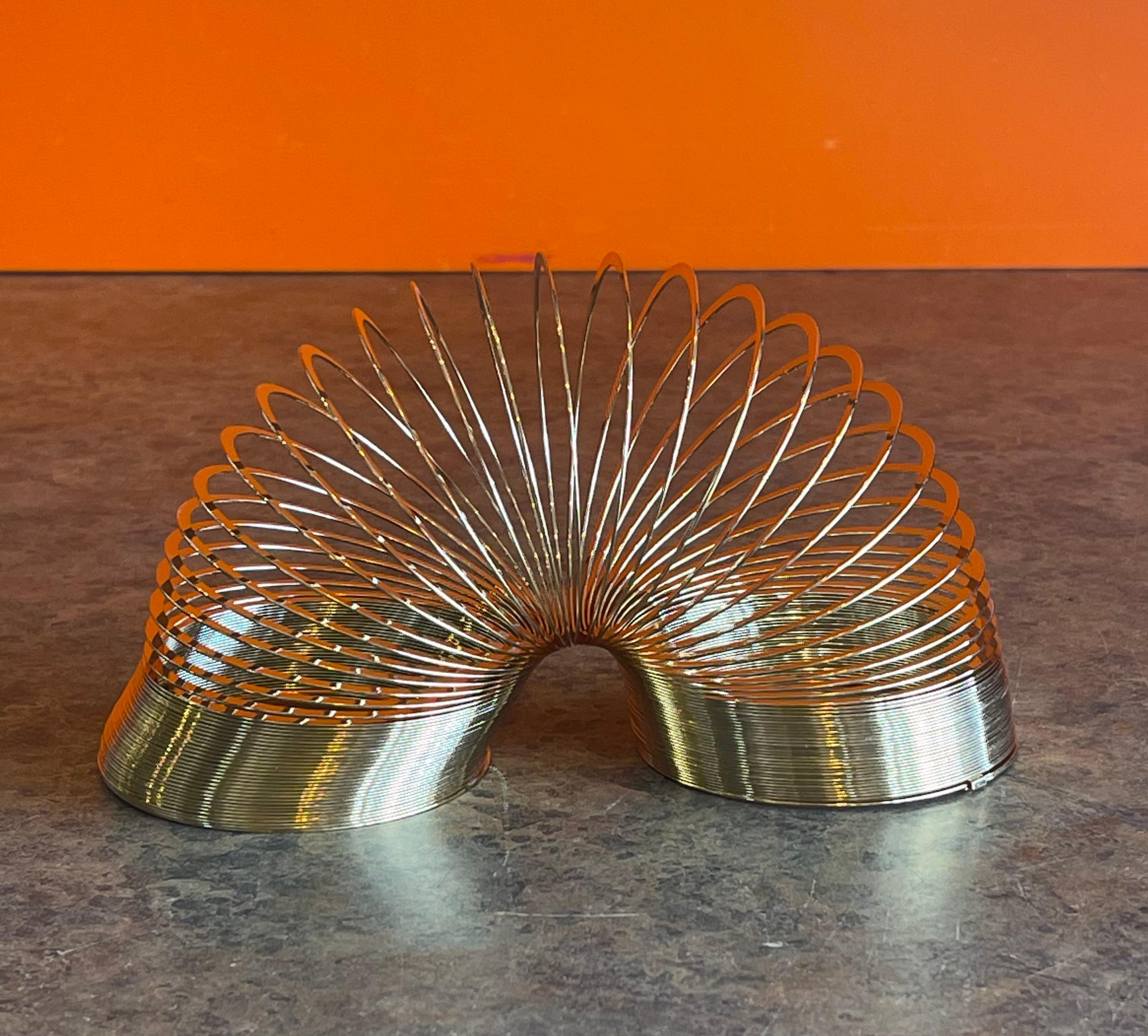 50th Anniversary gold-plated brass Slinky toy in wood box, circa 1995. This item is in very good vintage condition with minimal use and comes with the original brochure. The Slinky was released in 1995 to celebrate the toy's 50th anniversary; this