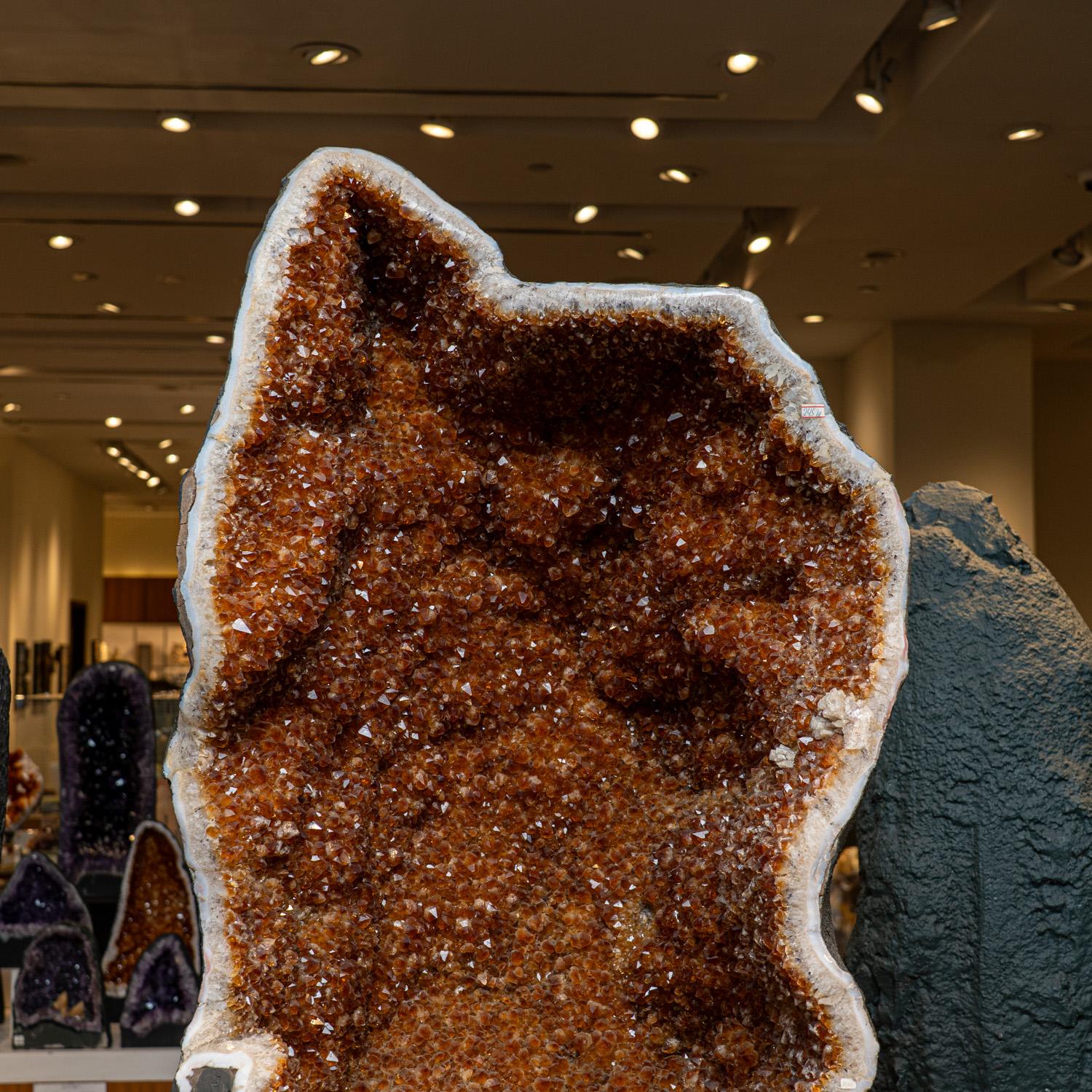 This Authentic Amethyst Cluster Geode from Brazil is a premium natural formation of gem amethyst adorned by small, smooth calcite crystals. The semi-geode cathedral decor showcases gleaming, fully terminated crystals with highly reflective surfaces