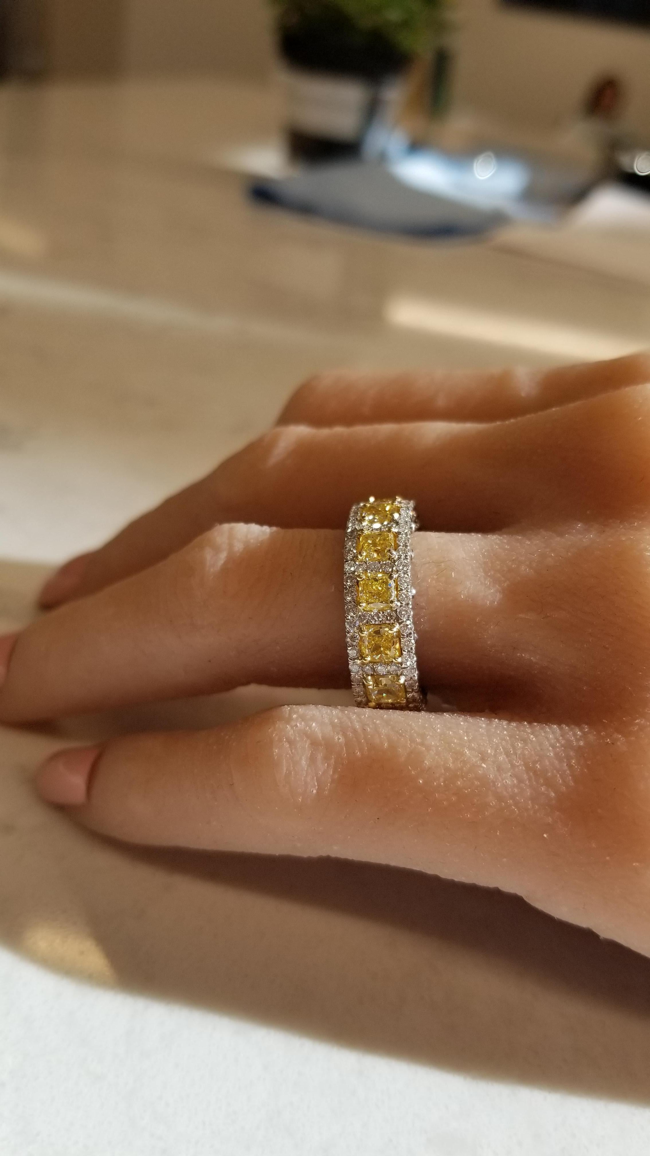 A total of 14 cushion cut natural fancy yellow diamonds are prong set all the way around the band totaling 5.10 carats and have VVS-VS clarity. The color of the cushion cuts are lemon yellow. Each of these natural fancy yellow diamonds is framed by