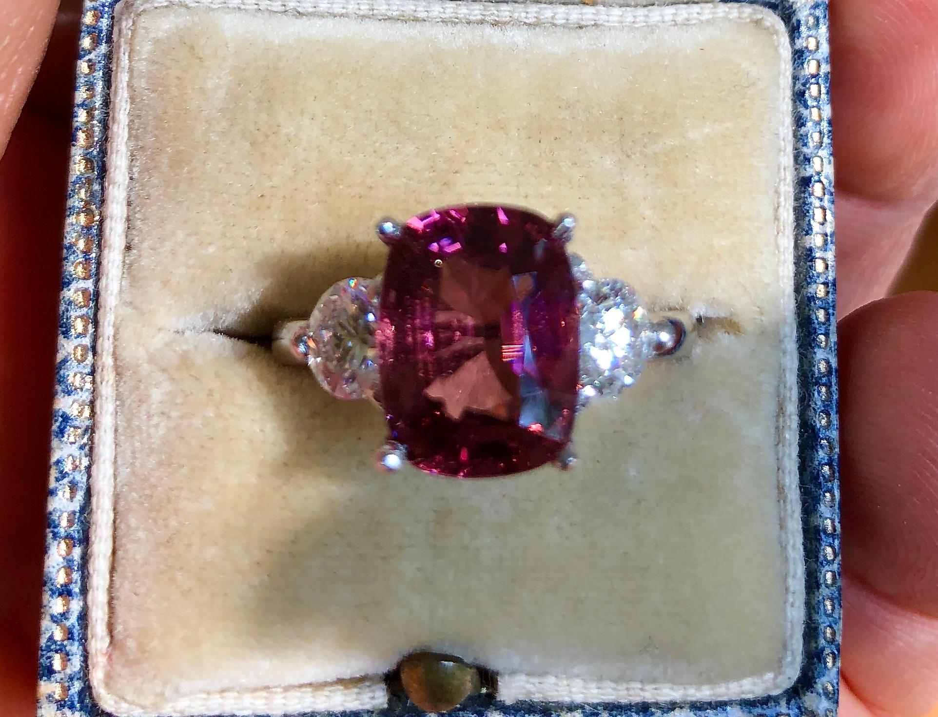 A vibrant purple-pinkish red 4.16 carat cushion-cut natural Spinel is the centerpiece of this ring. The vibrant gemstone is highlighted by two round brilliant cut diamonds weighing 0.94 carats, H-SI2-. This sparkling natural spinel has an amazing
