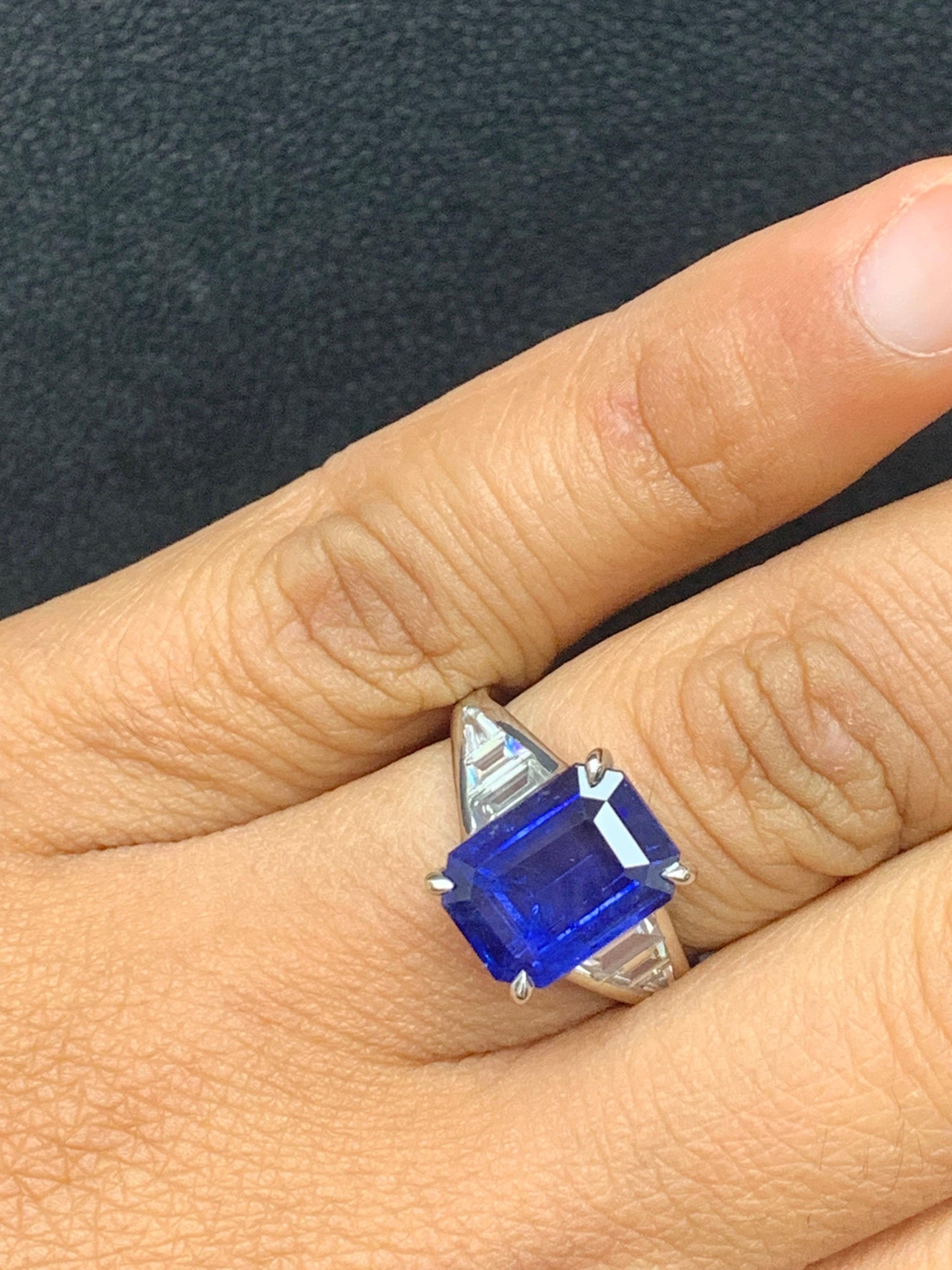 A stunning well-crafted engagement ring showcasing a 5.11-carat  emerald-cut Blue Sapphire. Flanking the center diamond are perfectly matched graduating step-cut diamonds, channel set in a polished platinum mounting. 6 Accent diamonds weigh 0.68