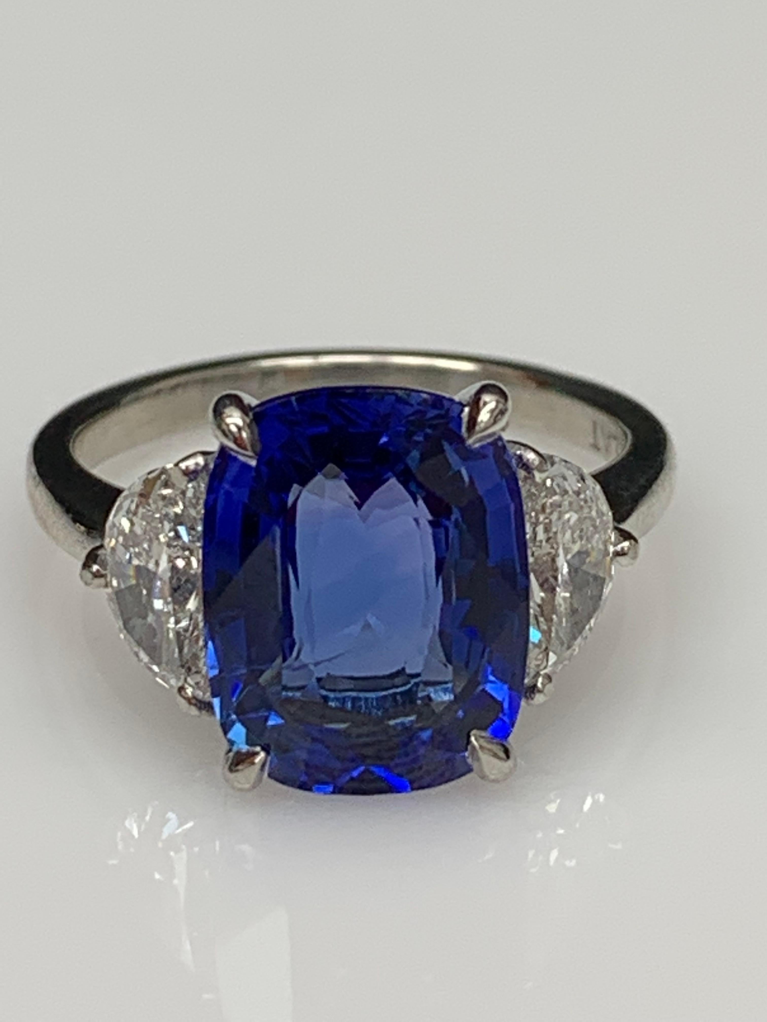 Showcases a Cushion cut, Vibrant color Blue Sapphire weighing 5.12 carats, flanked by two brilliant cut half moon diamonds weighing 0.89 carats total. Elegantly set in a polished platinum composition.