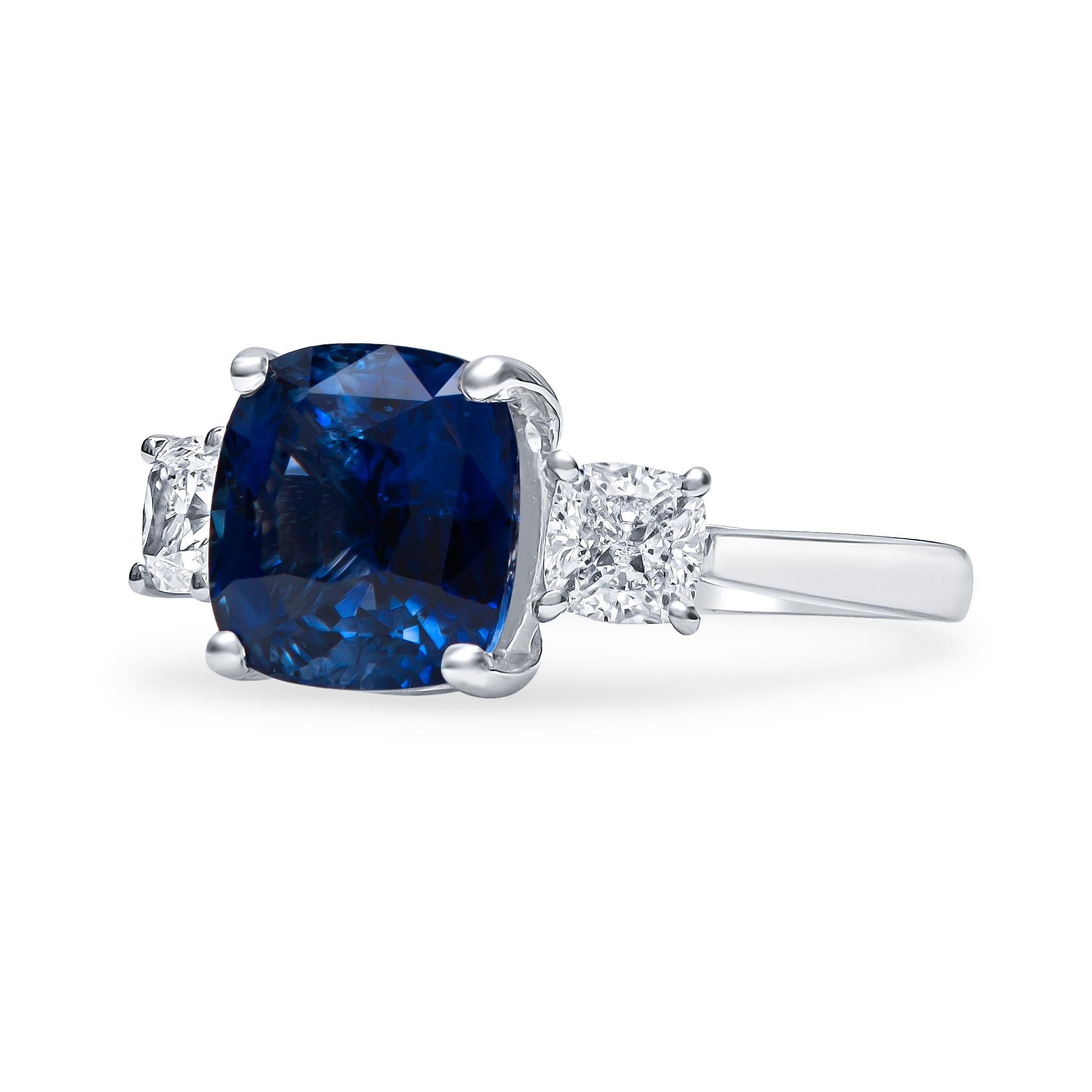 Captivating three-stone sapphire and diamond ring designed in platinum, showcasing a beautiful deep blue sapphire weighing 5.13 carats,  accompanied by two carefully selected and perfectly matched cushion cut diamonds weighing 1.02 carats total with