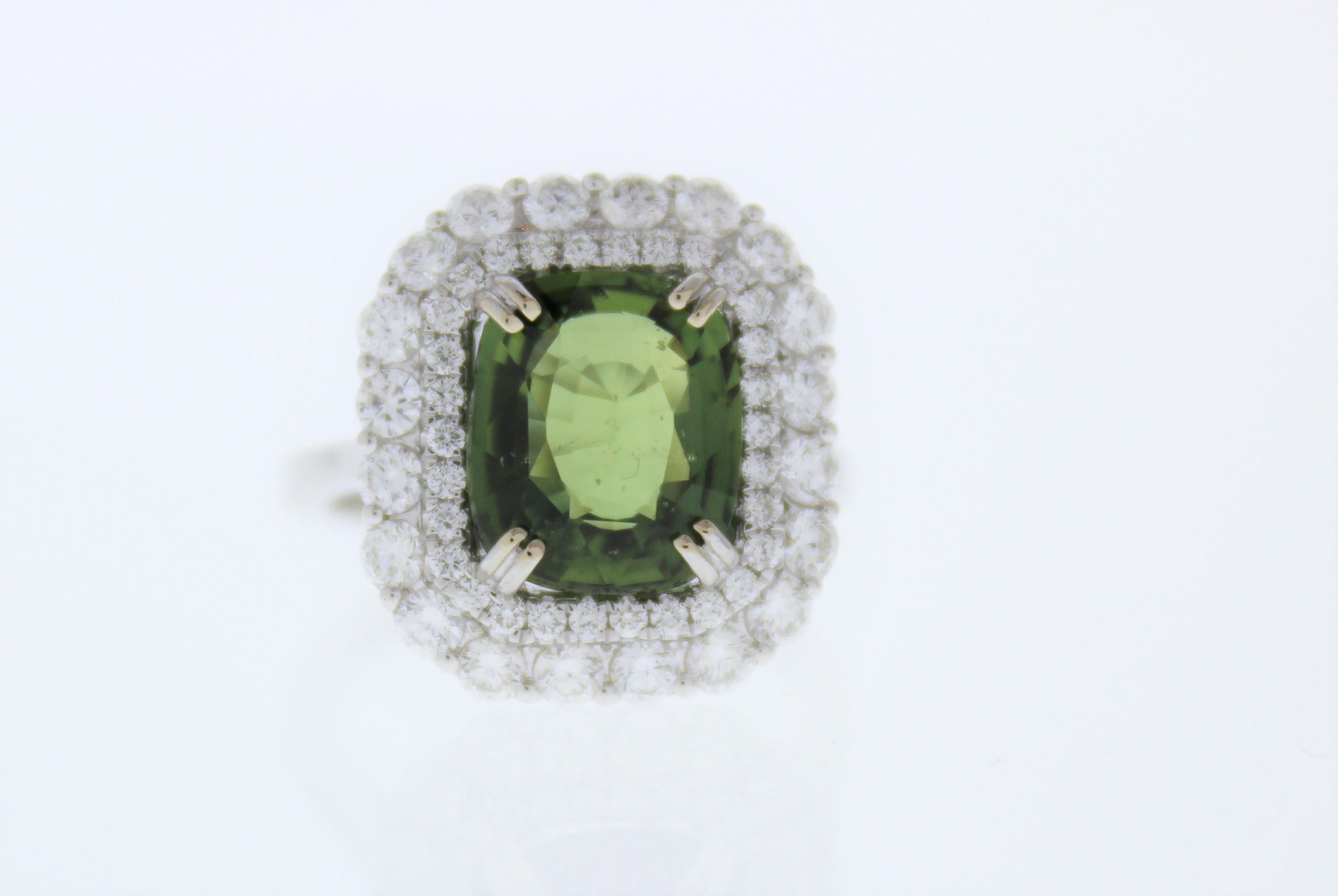 This unique halo cocktail ring features a cushion cut green sapphire weighing 5.13 carat. This green sapphire takes center stage in a rich gold double prong setting. Its gem source is Sri Lanka; its transparency and luster are excellent. A total of