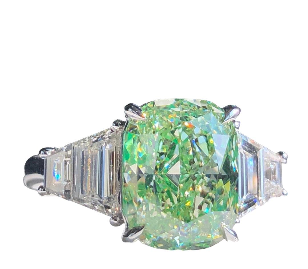 We invite you to discover this magnificent ring set with a GIA-certified fancy green cushion-cut diamond of 5.15 carats enhanced with 2 GIA-certified colorless Trapezoidal diamonds weighing 0.40 carats each. The wonderful vibrant green color of the