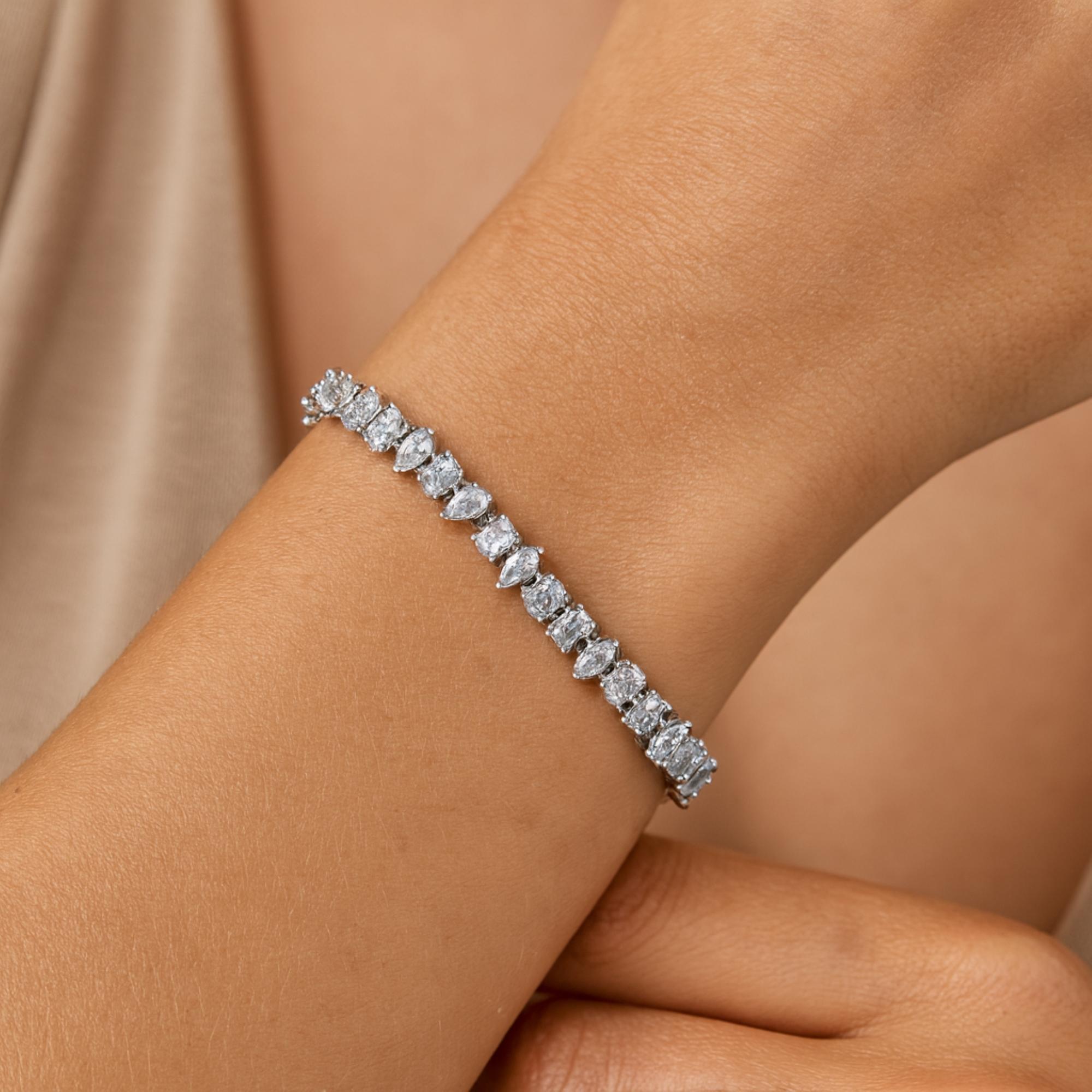 Esta pulsera de tenis de oro blanco de 18 quilates con diamantes naturales multiforma SI/H de 5,15 quilates presenta diamantes de talla mixta (pera, marquesa, oval, esmeralda) engastados en hilera formando una línea continua. 
Los diamantes son un