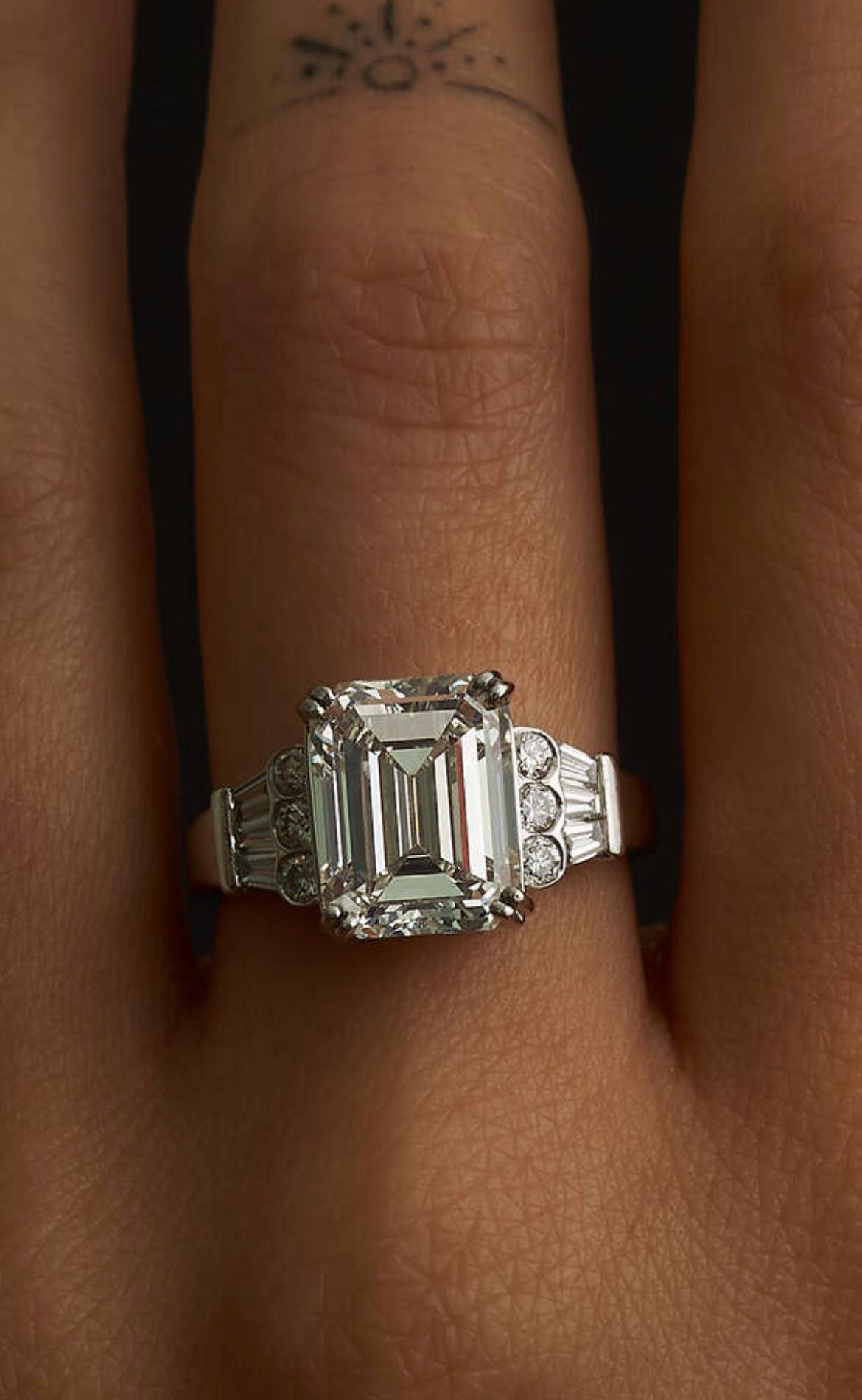 A 5.15 CARAT H COLOUR, VVS2 DIAMOND ENGAGEMENT RING in 18ct white gold, set with an emerald cut diamond of 5.15 carats, accented by trios of round brilliant and tapering baguette cut diamonds, full British hallmarks, size 0 / 7.25, 5.9g. Accompanied