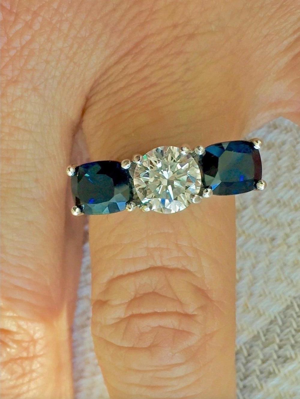 Questo splendido anello a tre pietre in oro bianco 18 carati presenta un diamante rotondo taglio brillante di 1,73 carati (purezza migliorata) al centro e due splendidi zaffiri naturali Royal blue taglio cuscino per un peso totale di 3,45 carati;