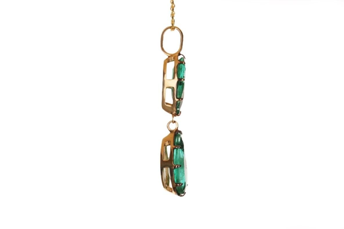 Displayed is an hourglass natural emerald Georgian styled solitaire pendant in 14K yellow gold. This gorgeous piece carries two emeralds in a prong setting. Black rhodium highlights the emeralds' bezel and prongs. Fully faceted, these gemstones
