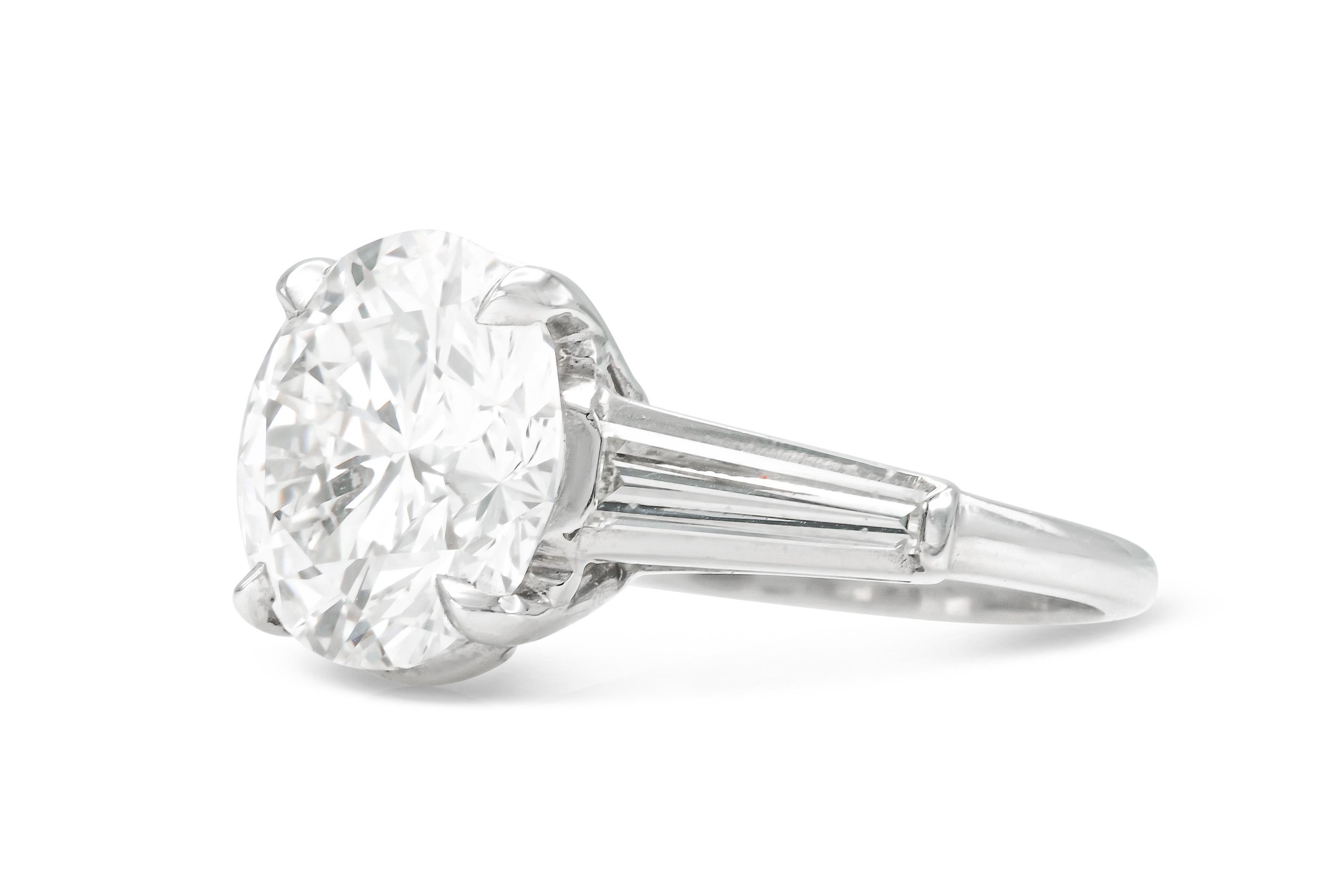 Fein in Platin gefertigt, mit einem GI-zertifizierten runden Diamanten im Brillantschliff mit einem Gewicht von 5,27 Karat, Farbe I, Reinheit VS1, GIA#16840246.
Der Ring ist mit 2 spitz zulaufenden Diamanten im Baguetteschliff verziert.
Größe 6 3/4,