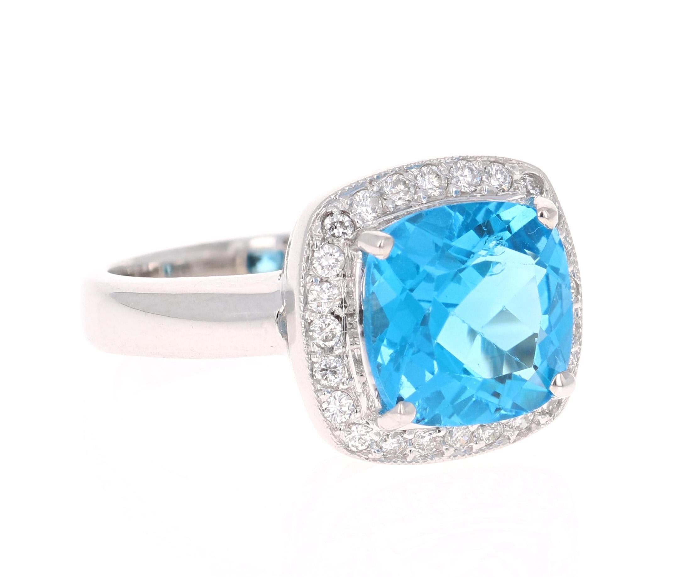 This stunning statement ring has a Cushion Cut Blue Topaz that weighs 4.96 Carats. 
It is surrounded by a simple halo of 24 Round Cut Diamonds that weighs 0.33 Carats. The clarity and color of the diamonds are SI-F. 

It is crafted in 14 Karat White