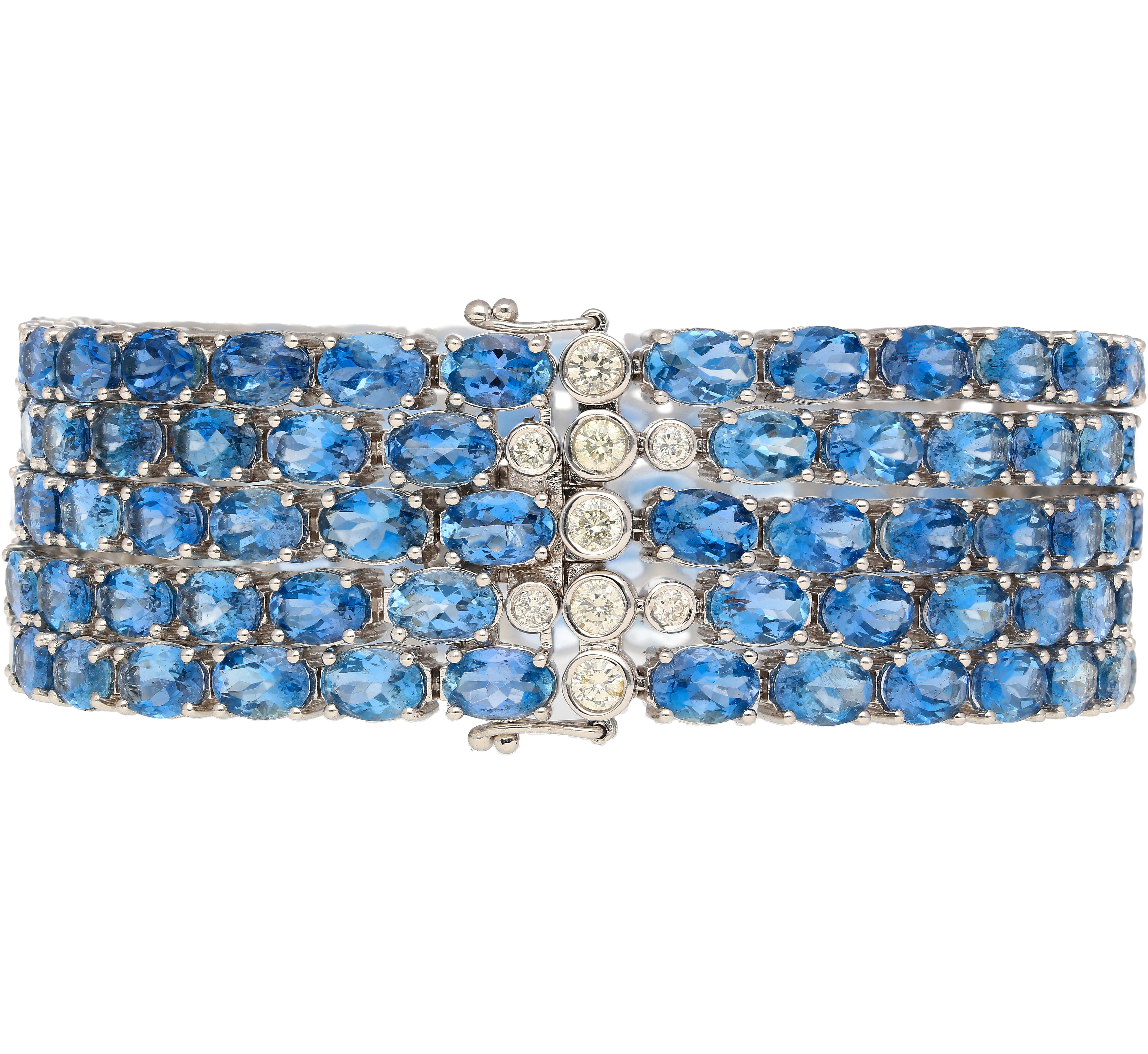 18k white gold aquamarine and diamond multi row link tennis bracelet. Featuring 5 rows of oval-cut aquamarines, with bezel set round cut diamonds on the closure. Bearing 129 aquamarines in 4-prong settings that dazzle a vibrant dance of ocean blue