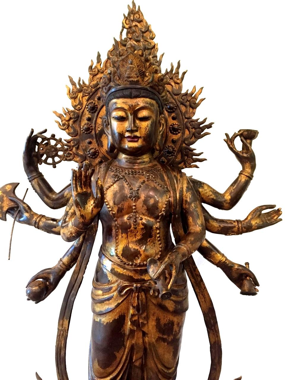 An exquisite bronze Multiple Armed Avalokitesvara Guan Yin statue. The 7-armed Goddess stands on double lotus throne, hands holding ritual objects including a lotus, mala pearl, ceremonial dagger, ambrosia vase, and Wheel of Law. Her broad Tang
