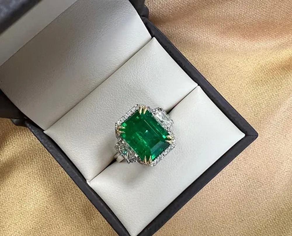 Emerald Weight: 5.30 CTS, Diamond Weight: Trapezoid side stones 0.73 CTS (I-VS), Halo 0.14 CT, Metal: Platinum/18K Yellow Gold Basket, Gold Weight: 8.19 gm, Ring Size: 7, Shape: Emerald-Cut, Color: Intense Green, Hardness: 7.5-8, Birthstone: May, CD